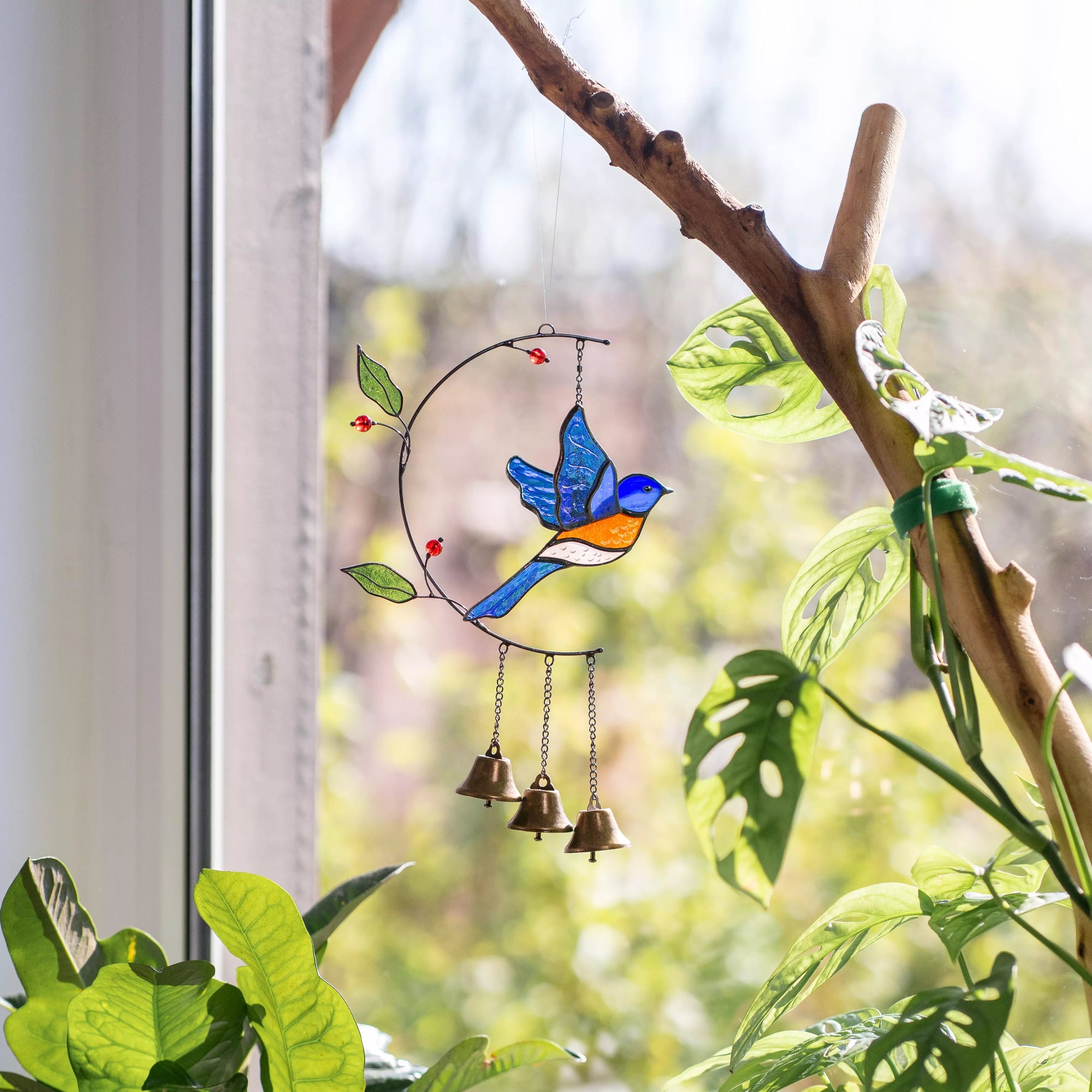Decorative stained glass bluebird wind chime with bells hanging on a branch indoors.