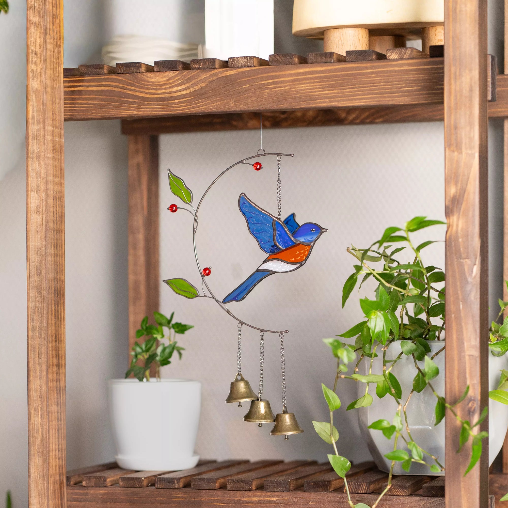 Stained glass bluebird wind chime with bells on a wooden shelf with plants