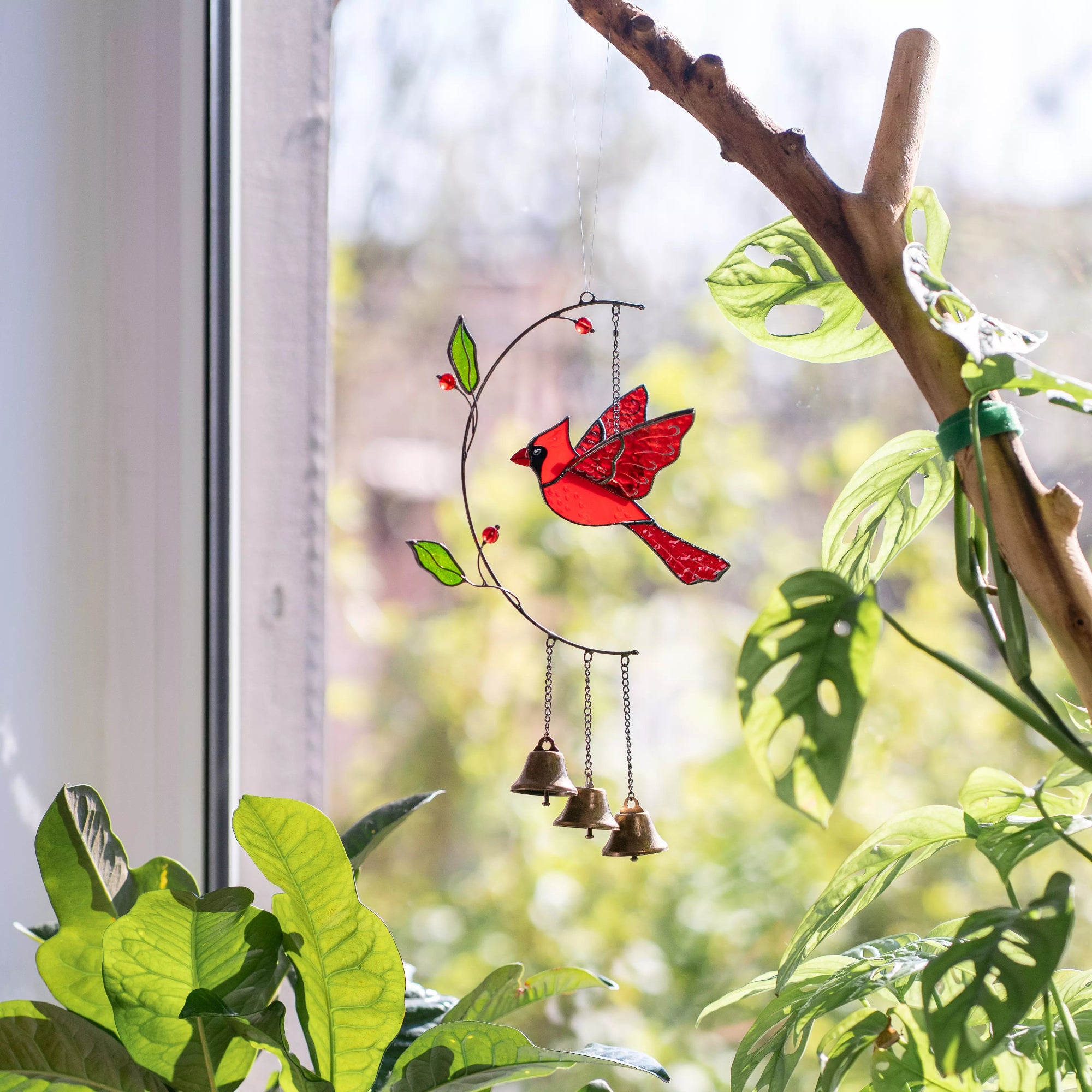 Decorative stained glass cardinal wind chime on a branch with leaves in the background