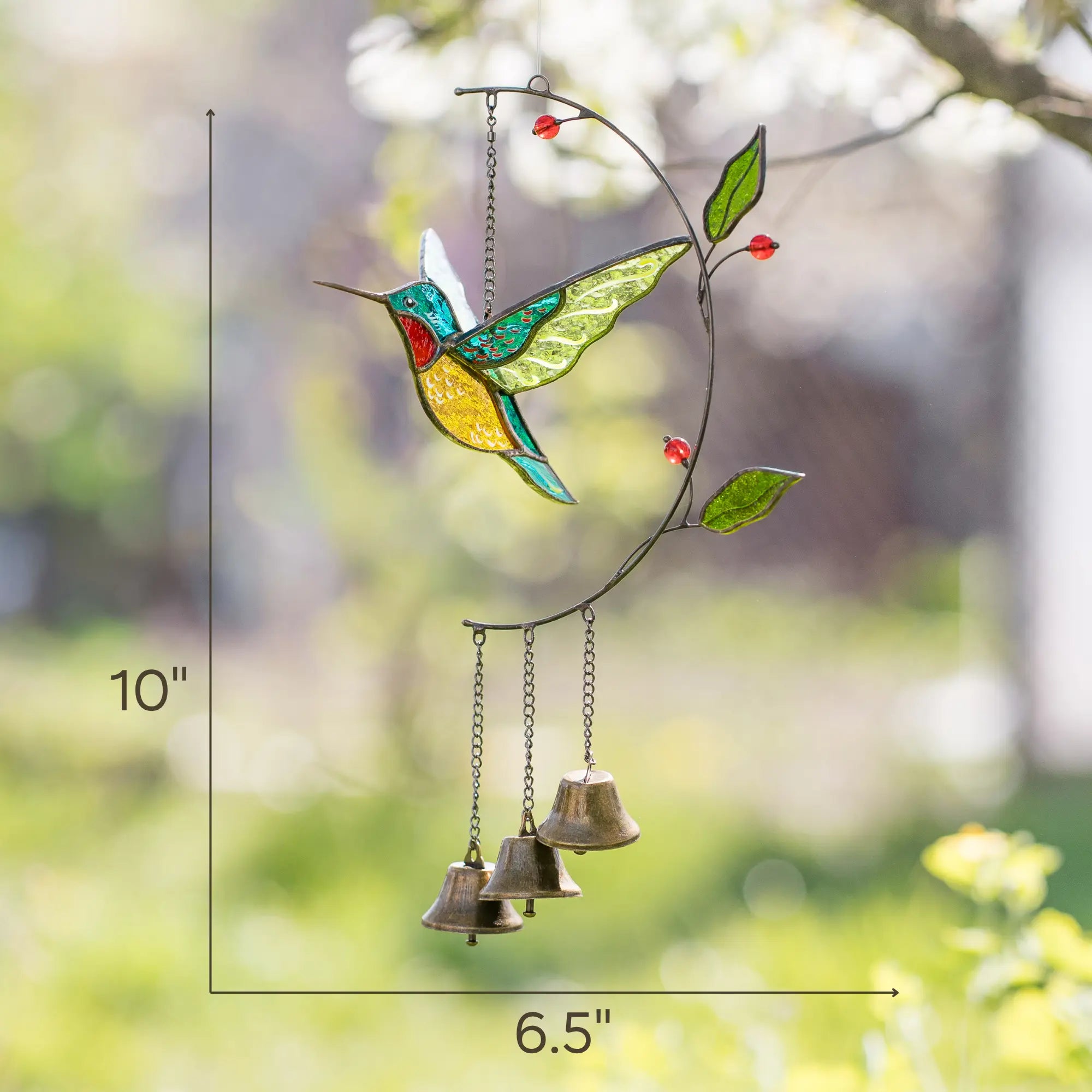 Stained glass hummingbird with bells on a branch against a blurred natural background