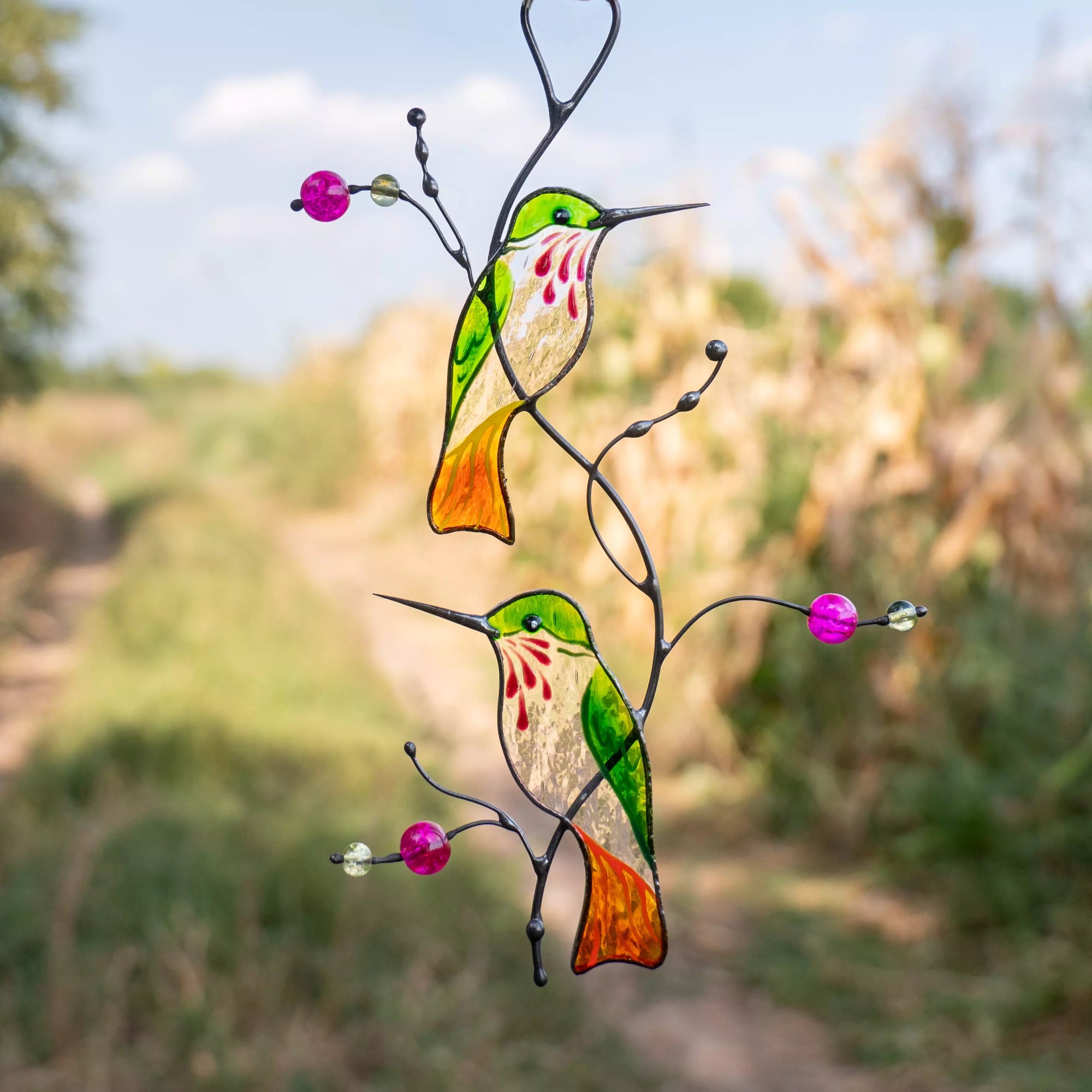 Stained glass hummingbirds on a branch with flowers against a natural background