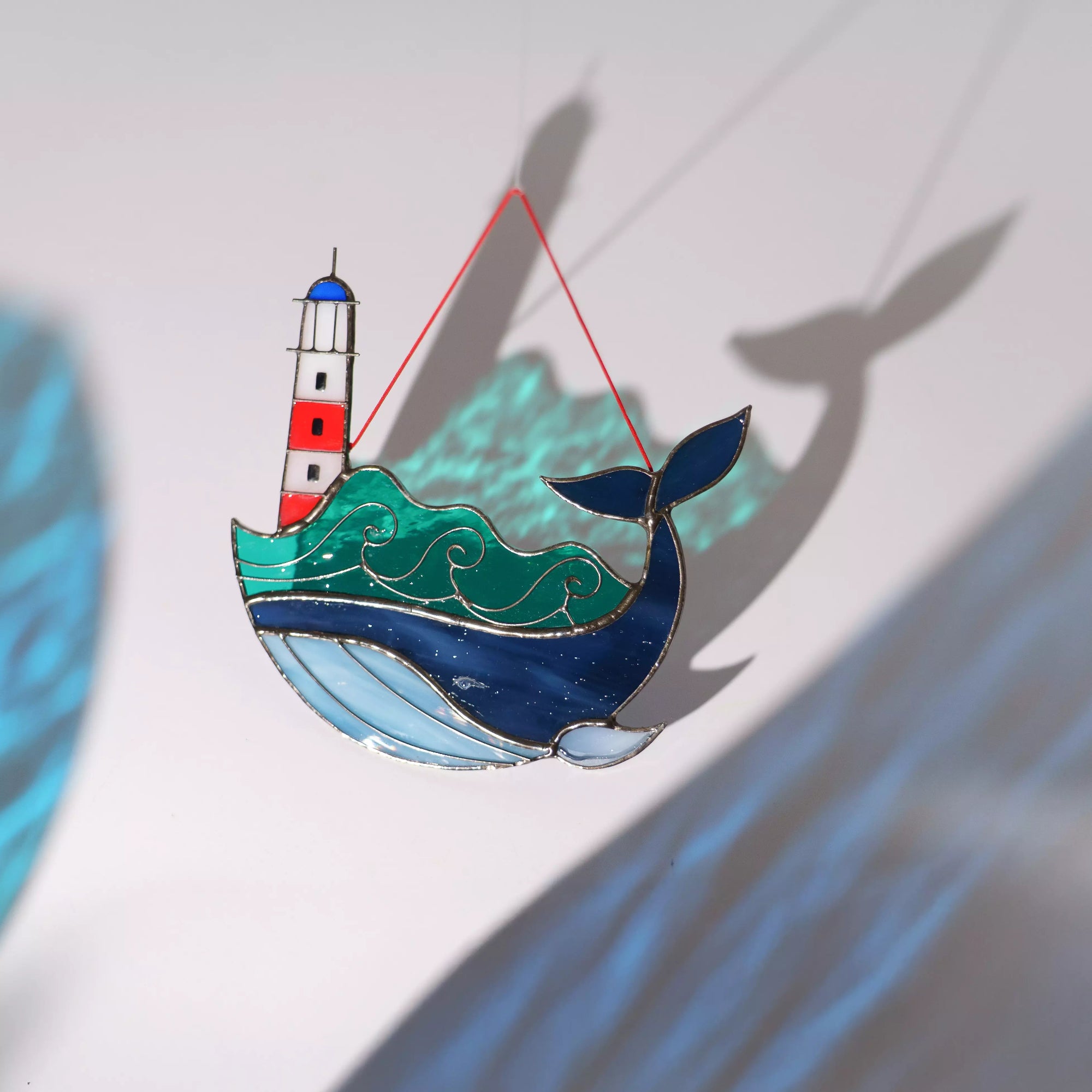Stained glass suncatcher whale with a lighthouse casting a colorful shadow on a surface