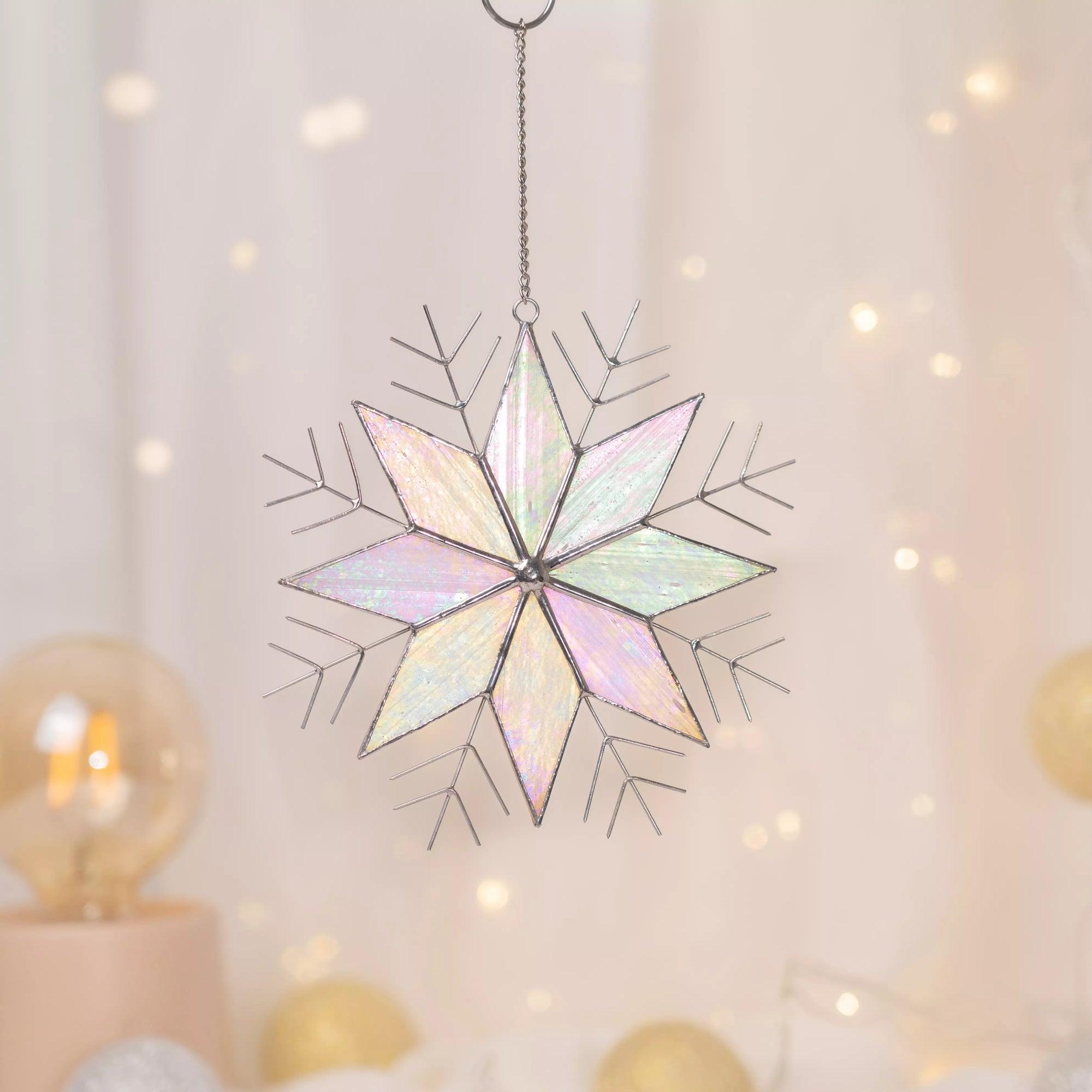 Stained glass snowflake suncatcher hanging against a soft, blurred background with lights.