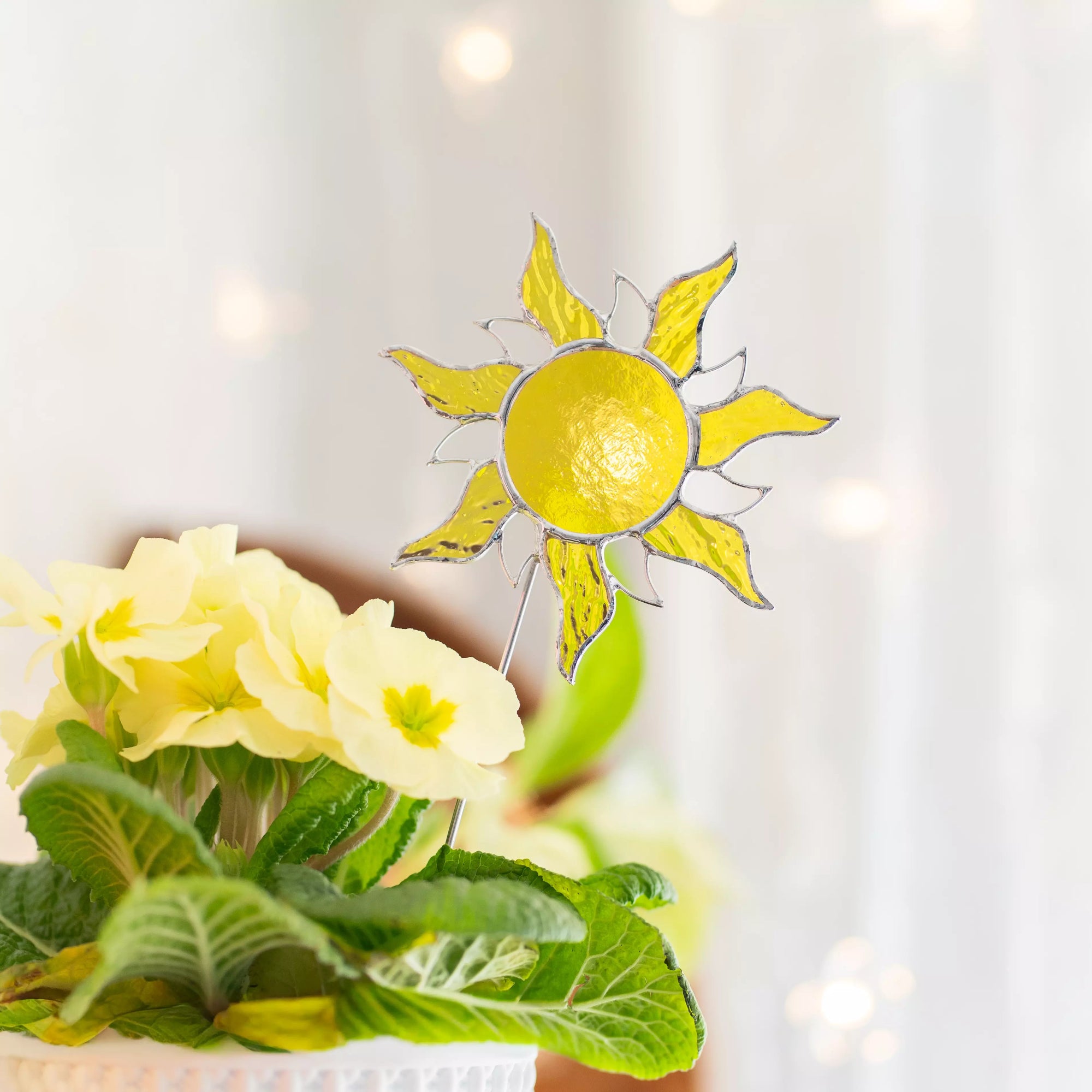 Stained glass sun plant stake on a plant with a blurred light background