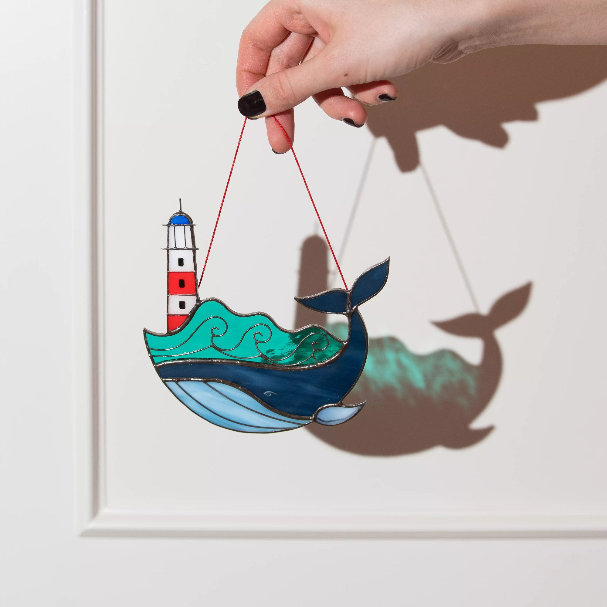 Stained glass whale with a lighthouse on a string against a white background