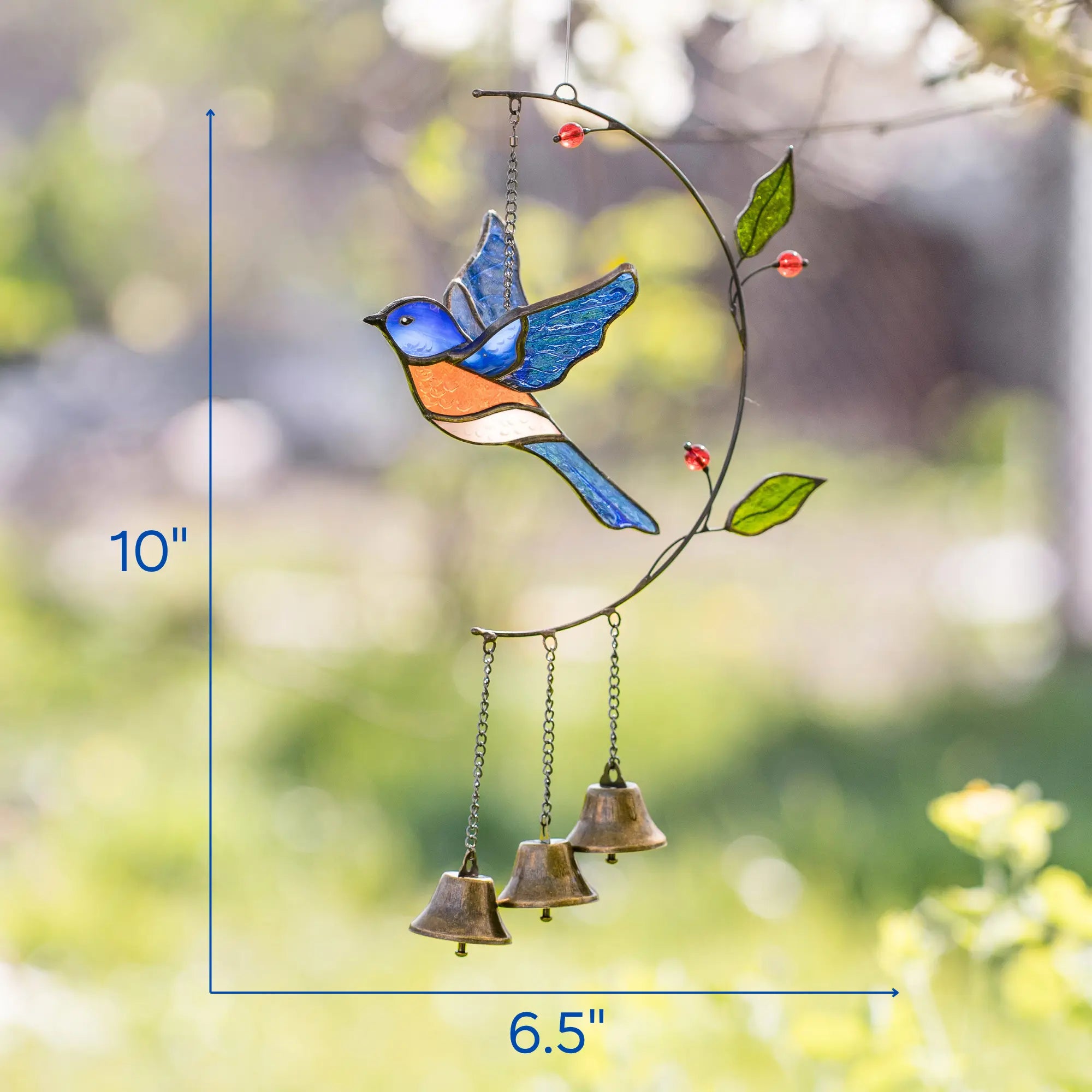 Stained glass wind chime with a bird design and bells, set against a blurred natural background with dimensions: 6.5 x 10 inches