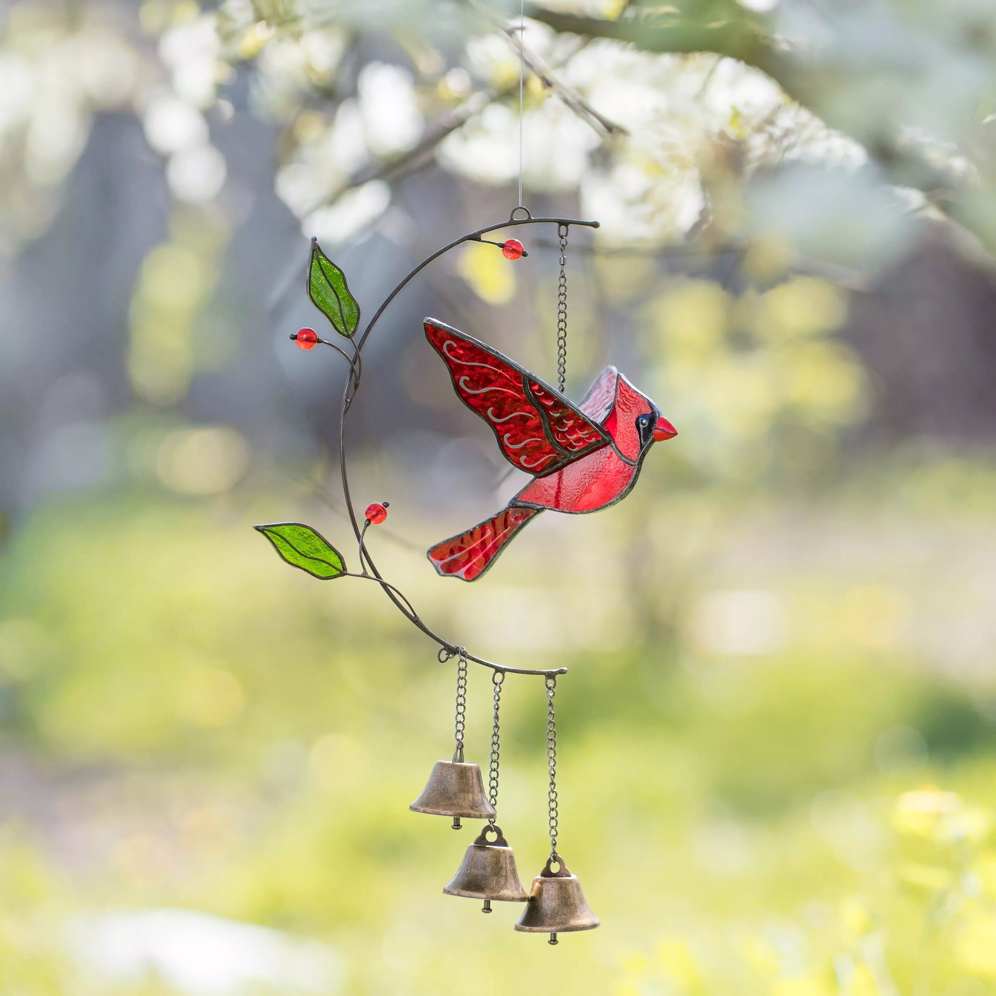 Stained glass wind chime with a red bird design hanging against a blurred natural background
