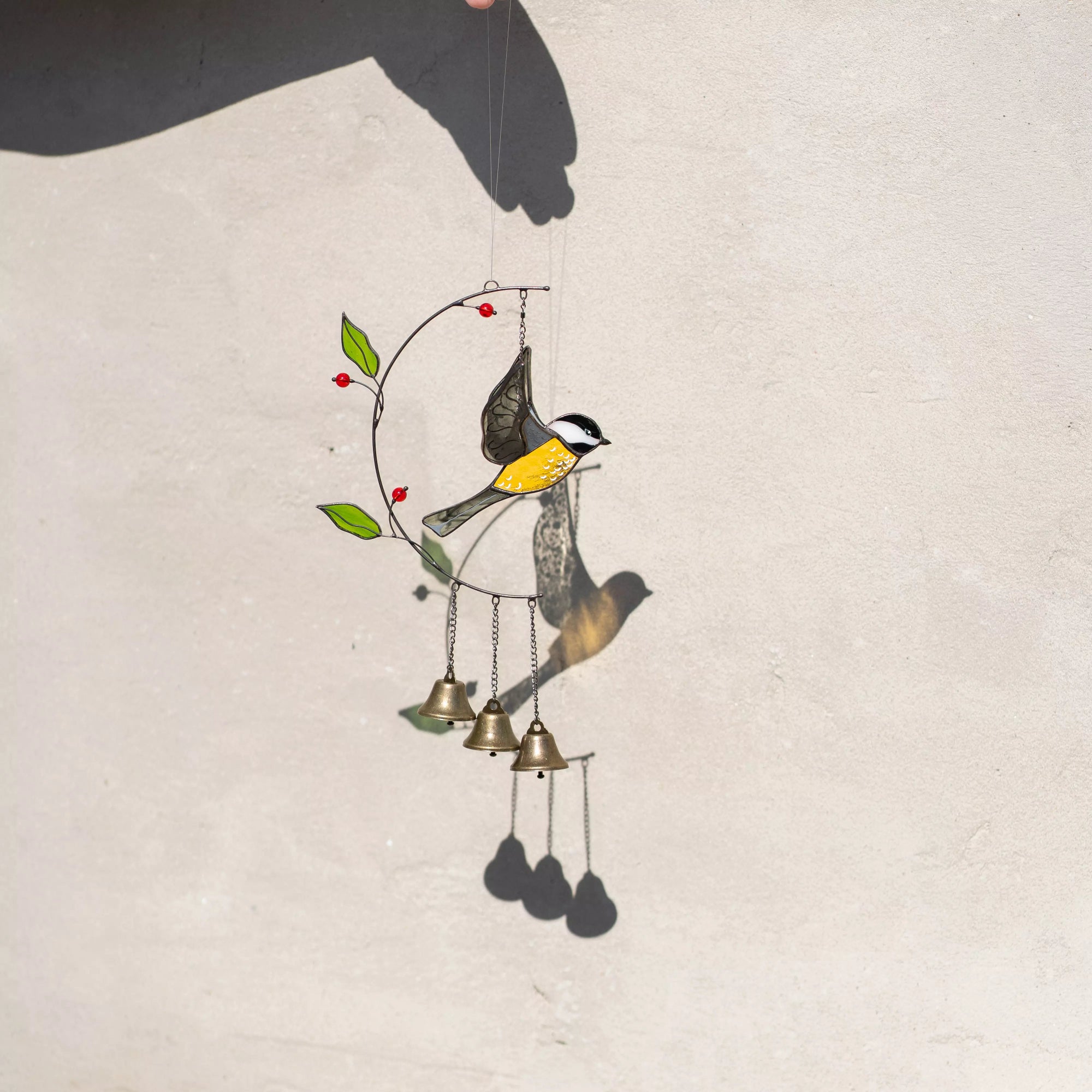 Stained glass wind chime with chickadee design on a light background casting a soft shadow