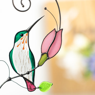 Glass hummingbird beak reaching toward pink flower, highlighting handmade stained glass details.