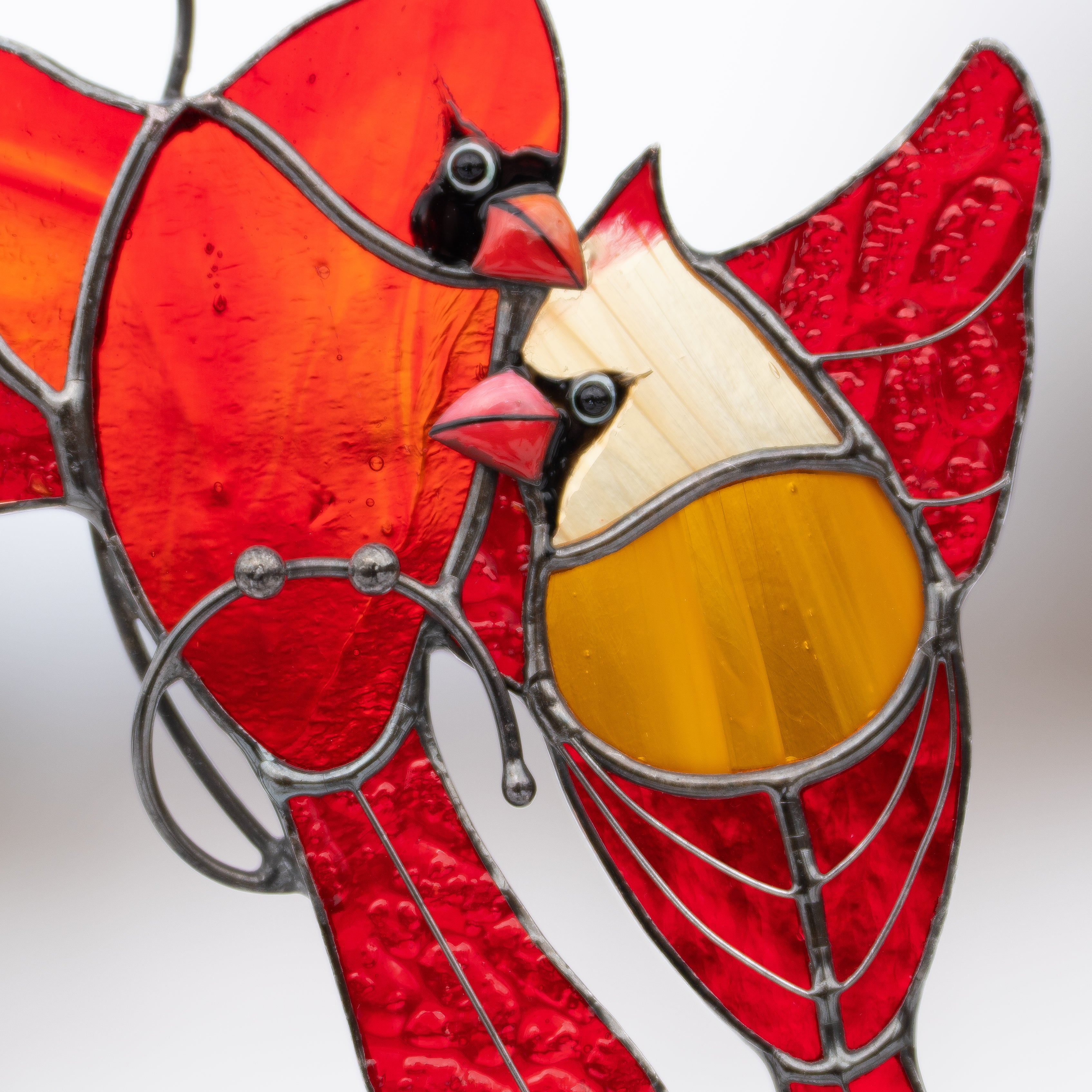 Close-up of stained glass cardinal faces with intricate soldering and vivid colors.
