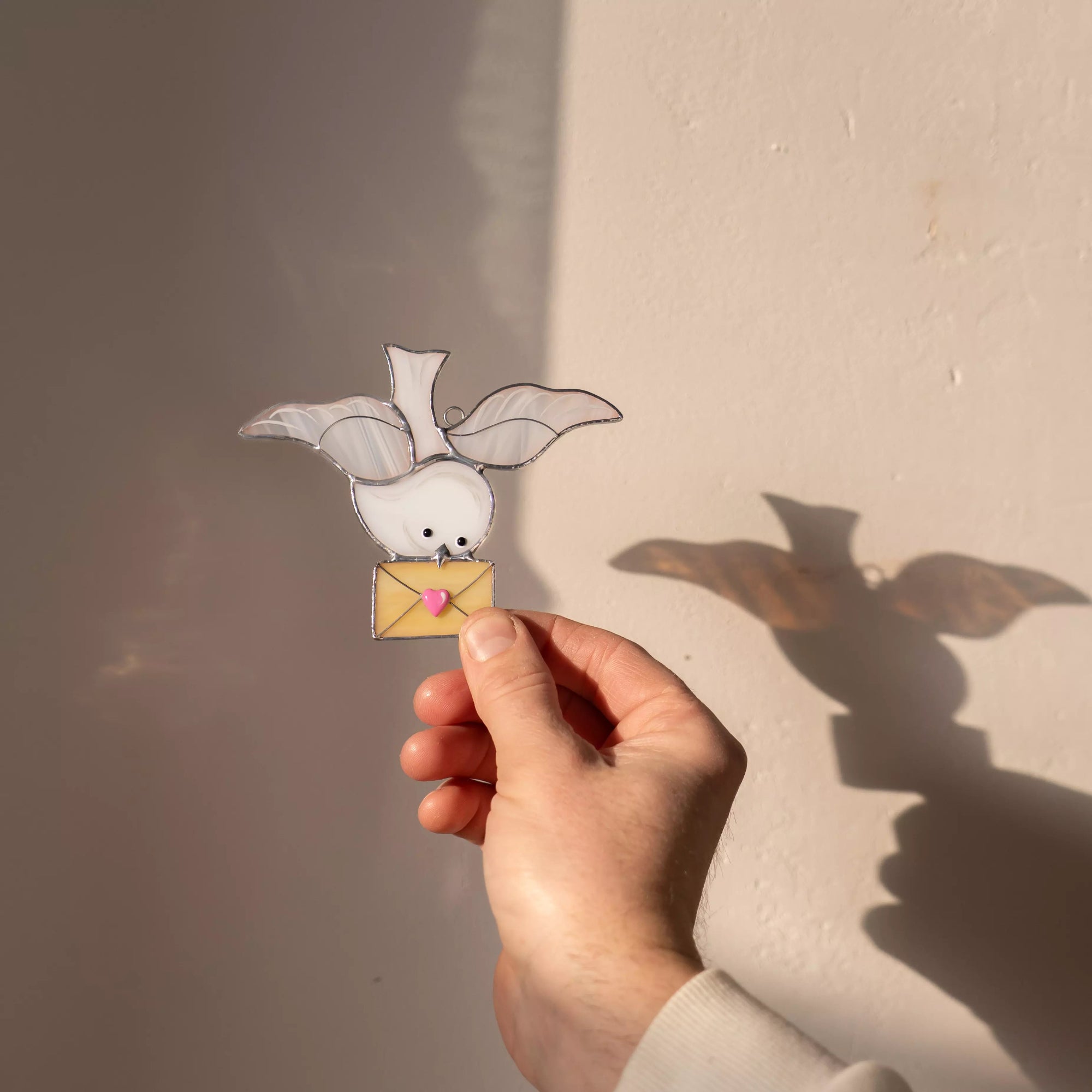 Dove stained glass suncatcher catching sunlight and casting a soft bird-shaped shadow on the wall.