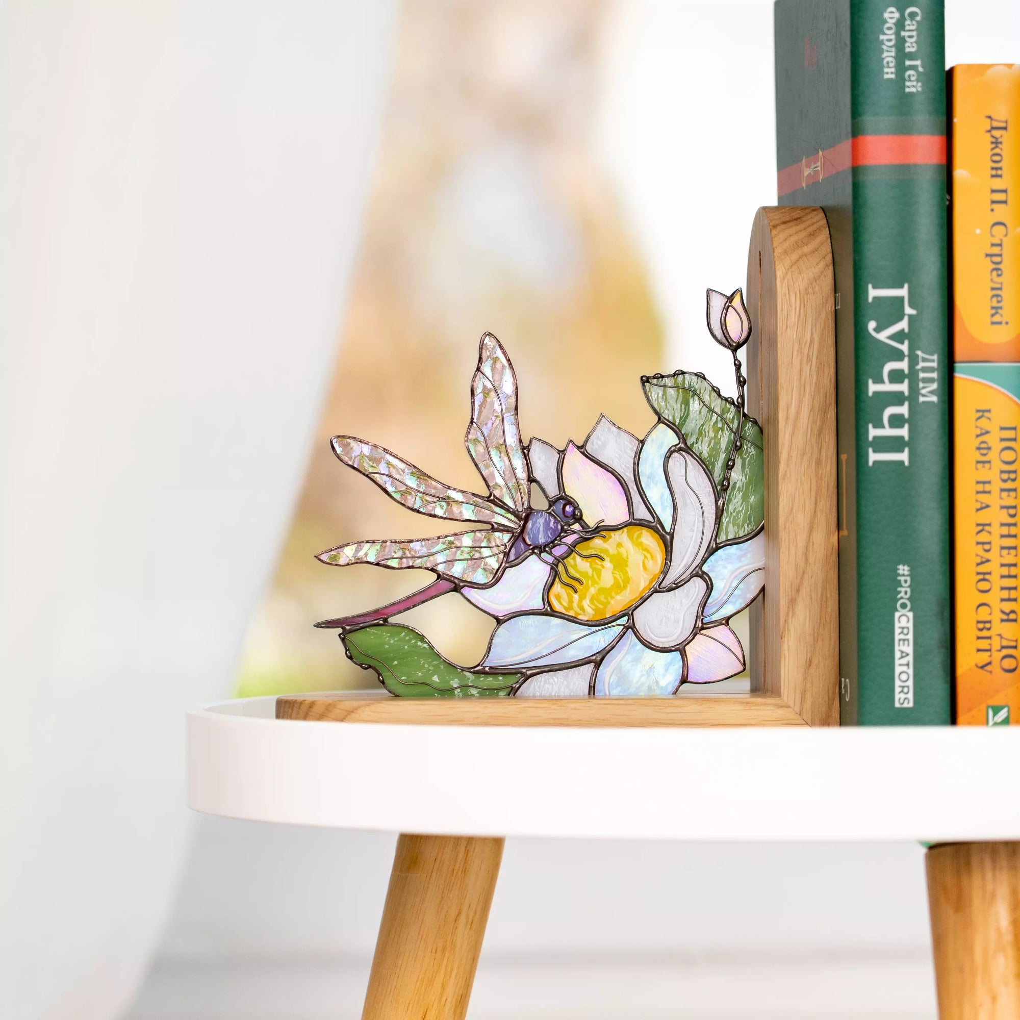 Stained glass dragonfly and flower panel displayed as a decorative bookend on a shelf.