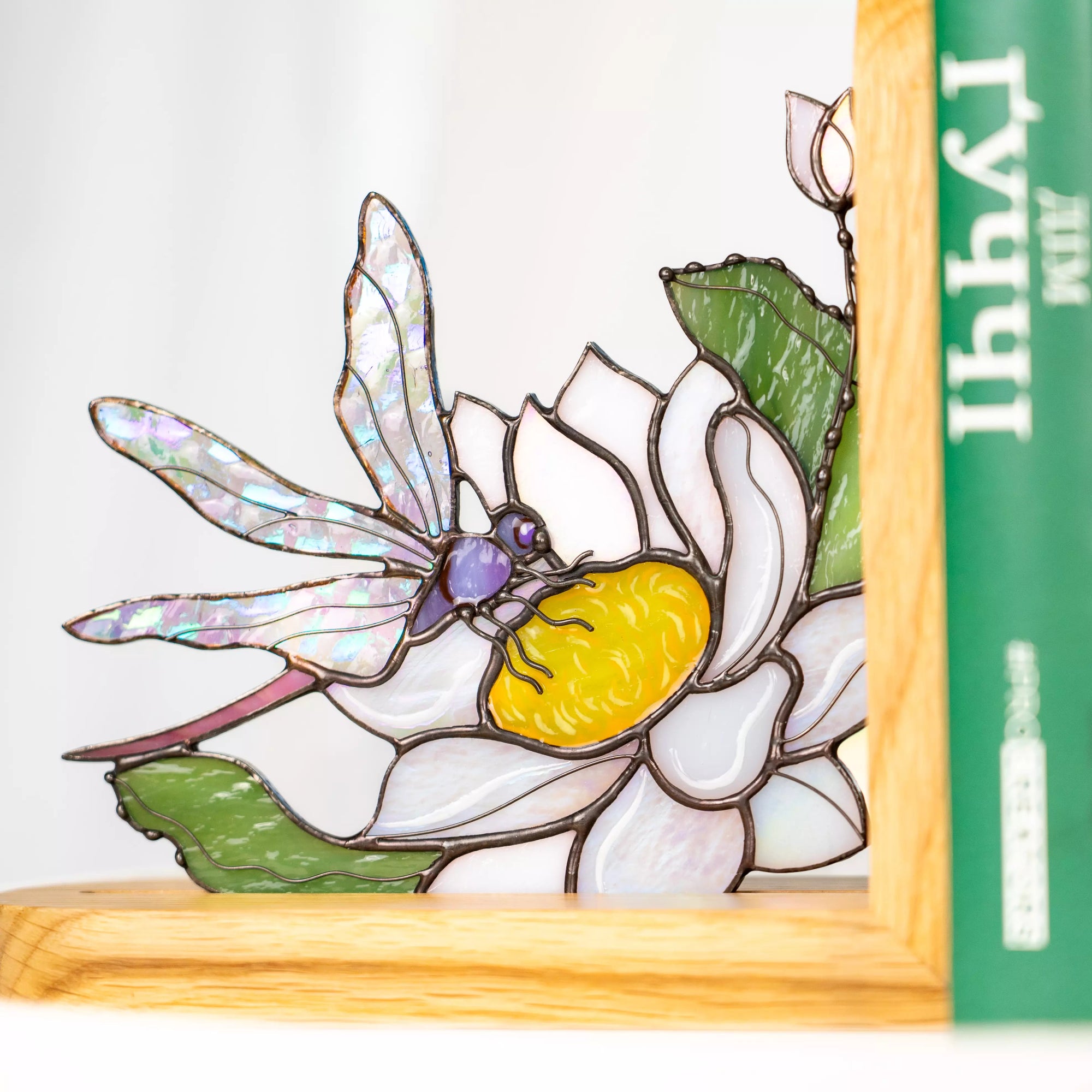 Close-up view of a stained glass dragonfly resting on a blooming flower, shown in a wooden stand.