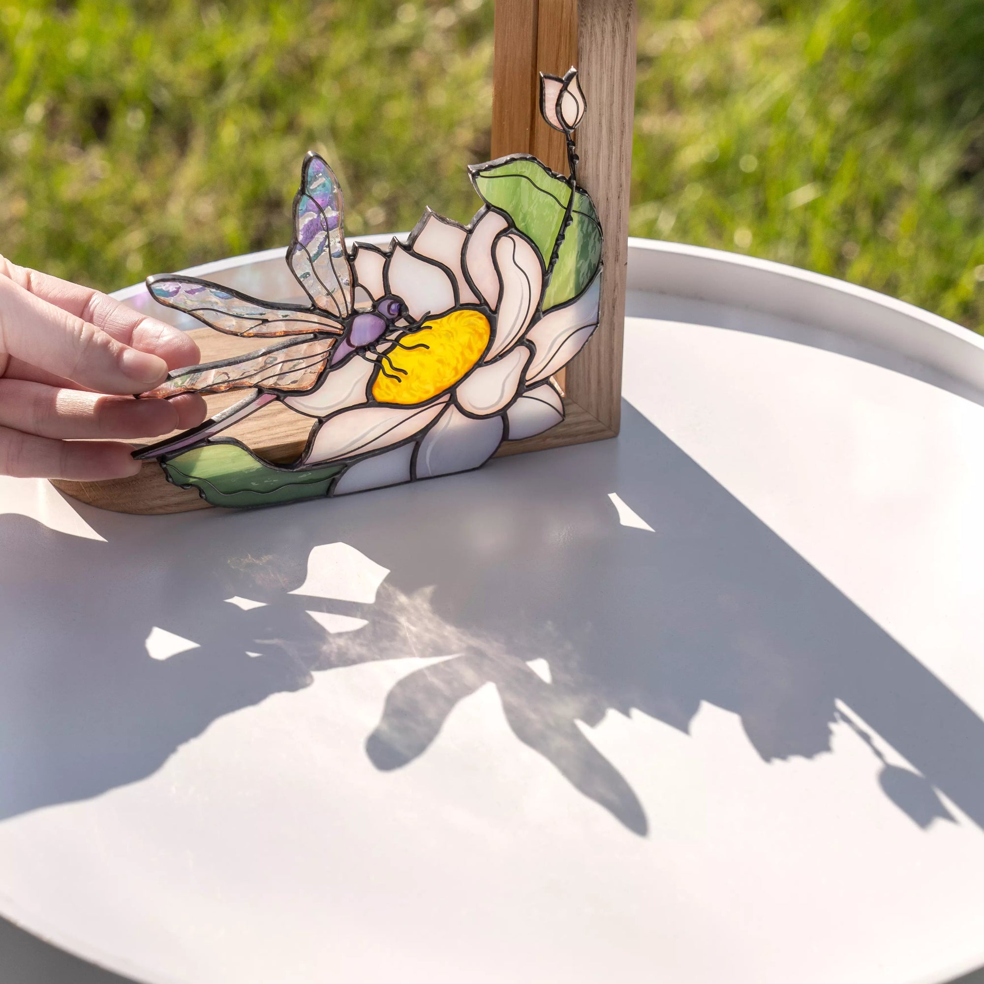 Dragonfly stained glass flower panel shown in bright sunlight, casting organic shadows on a surface.