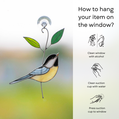 Yellow and gray stained glass chickadee with green leaves hanging on a window using a suction cup.