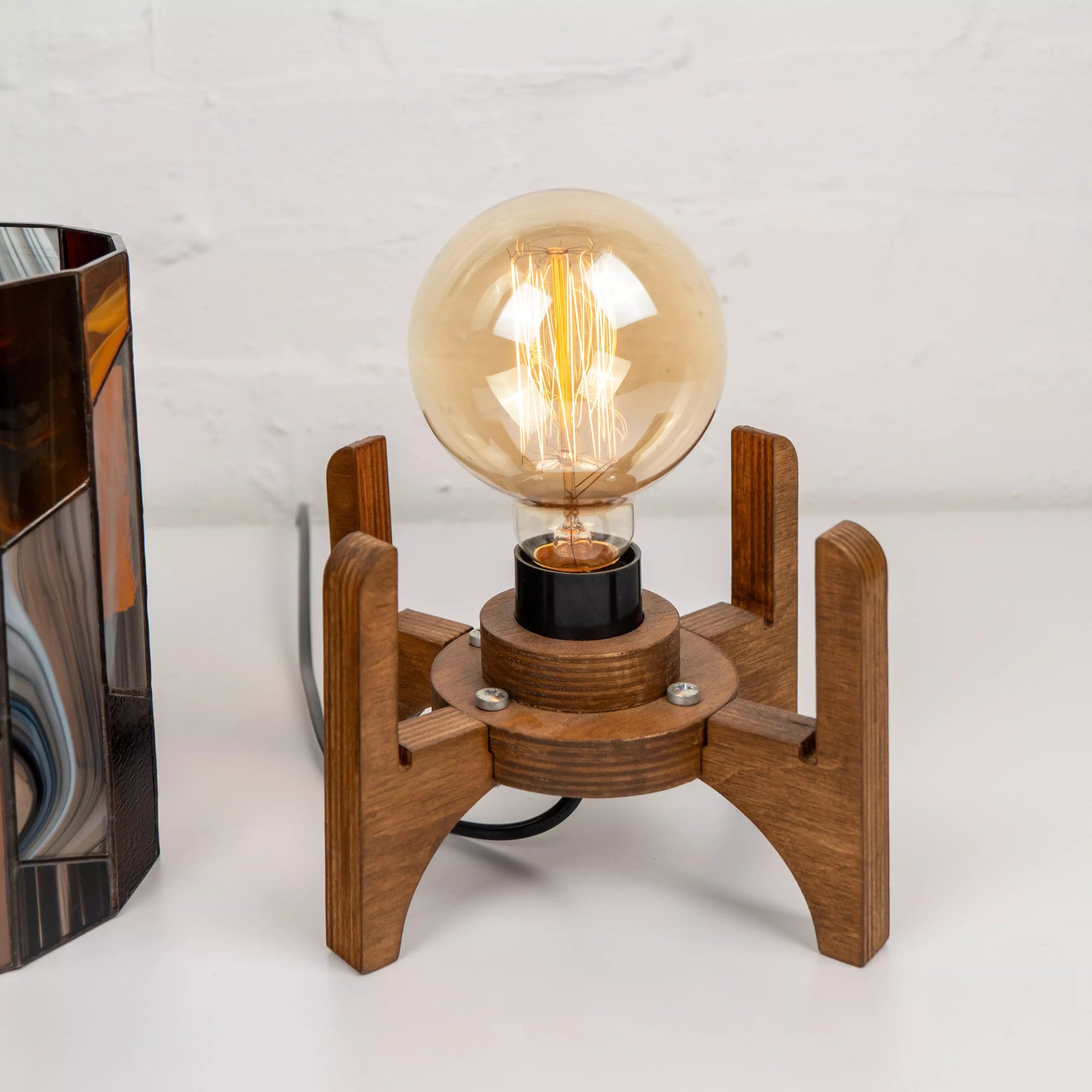 Close-up of Edison bulb inside stained glass lamp on a handcrafted wooden base, showing natural materials and warm glow.