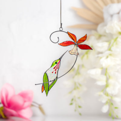 Hummingbird suncatcher with red bell flower surrounded by white and pink background flowers.