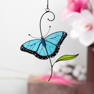 Stained glass morpho butterfly with deep blue wings and a green leaf accent.