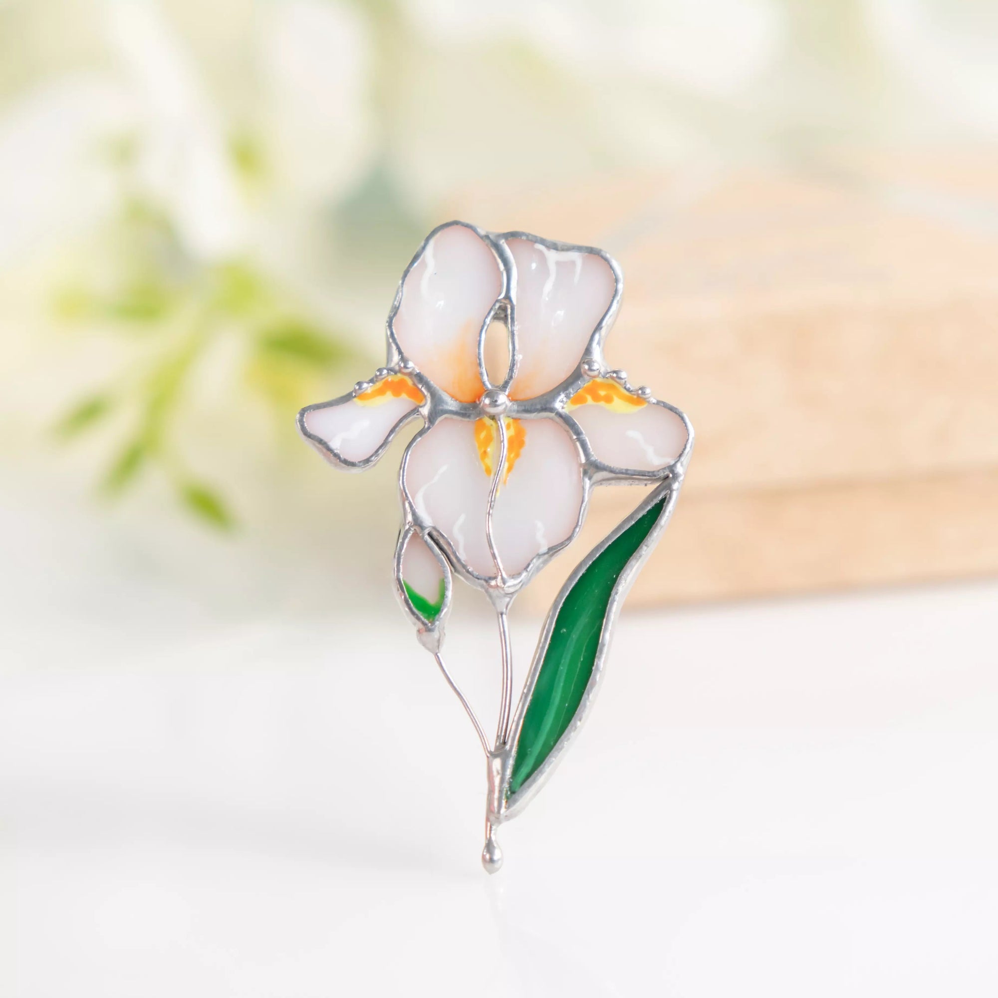 Stained glass brooch shaped like an iris flower, white petals with yellow details, standing upright.