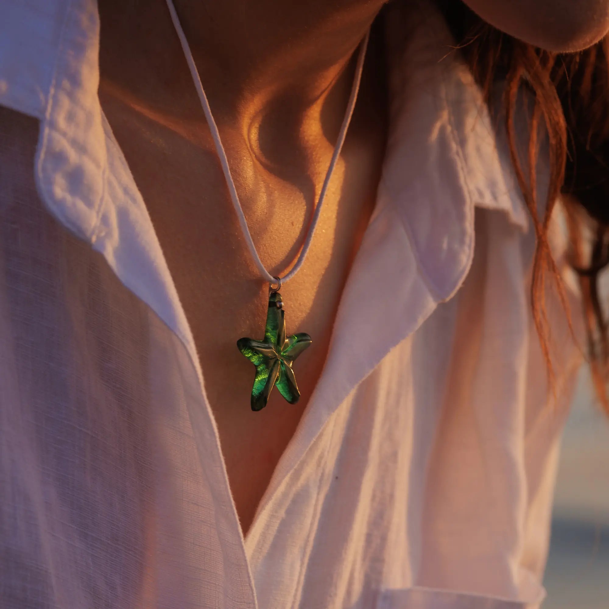 Green glass starfish pendant on a white cord, worn over a white linen shirt in evening light.