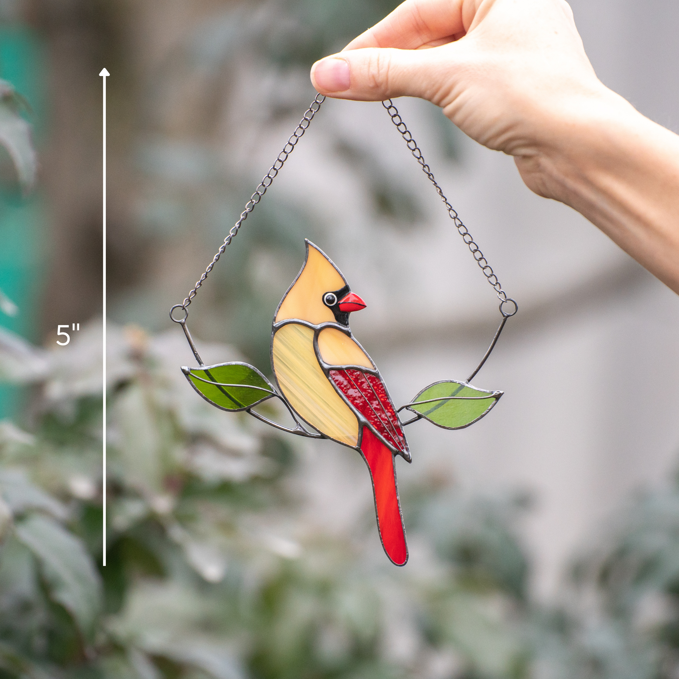 Stained glass female cardinal held by hand with blurred outdoor foliage in the background
