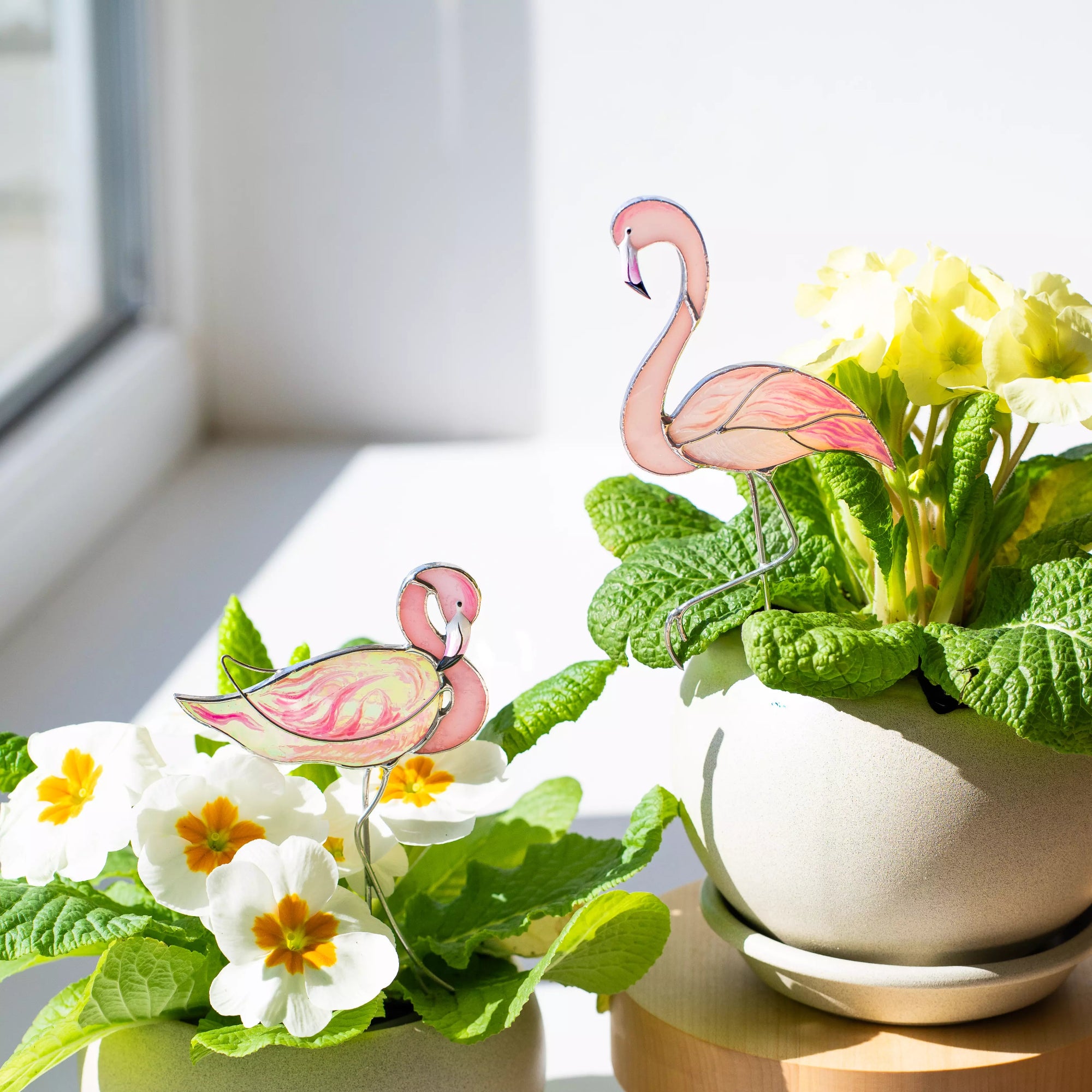 Flamingo stained glass plant stakes in a pot of flowers near a window