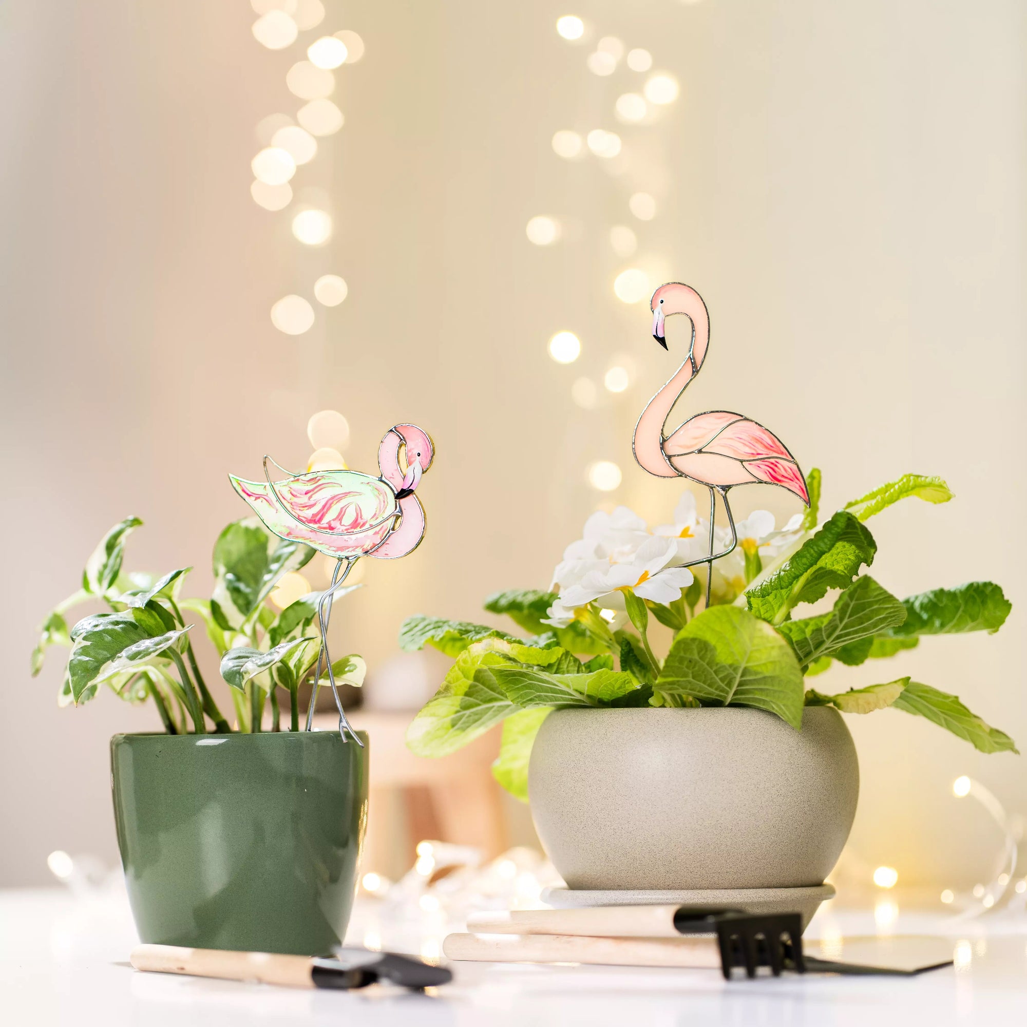 Flamingo stained glass plant stakes in pots with a blurred light background
