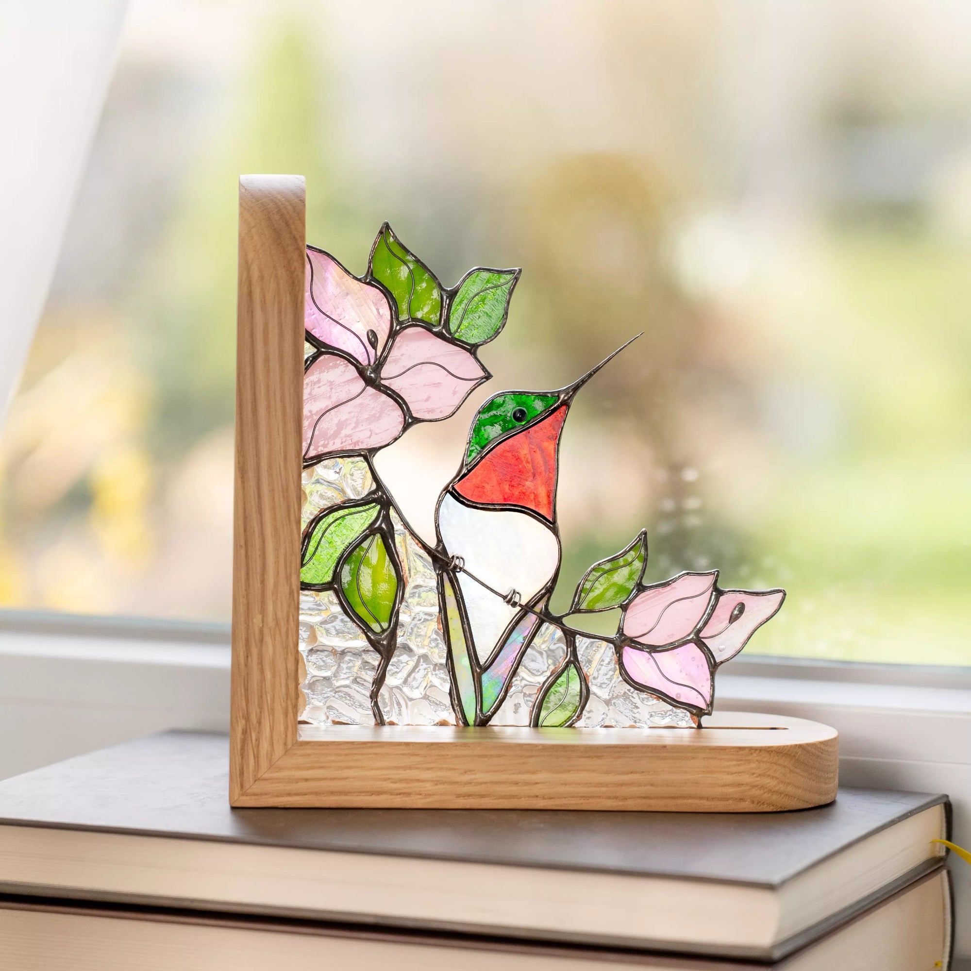 Decorative stained glass hummingbird bookend with pink blossoms and green leaves on a wooden base.