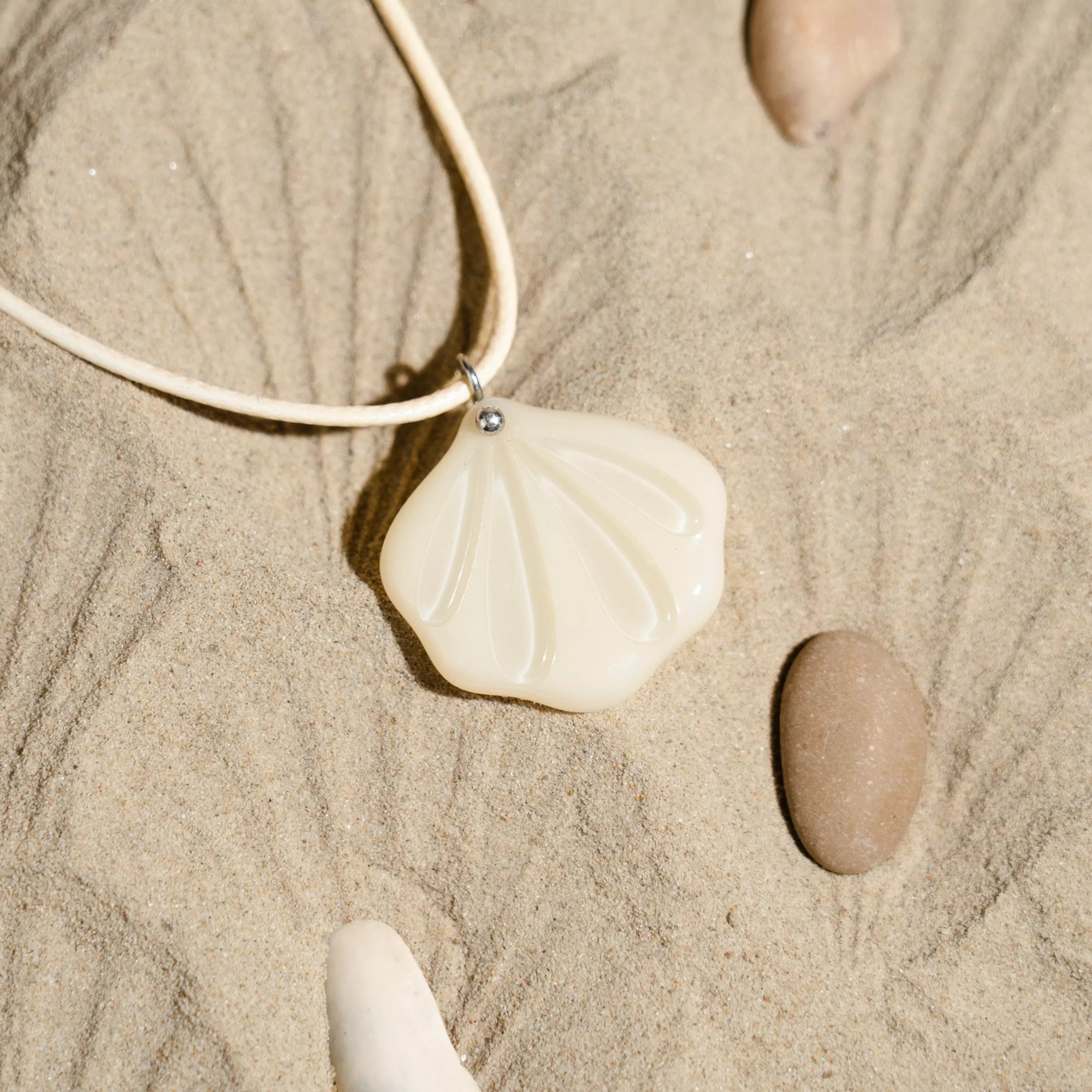 Necklace with a fused glass ivory shell pendant on sand