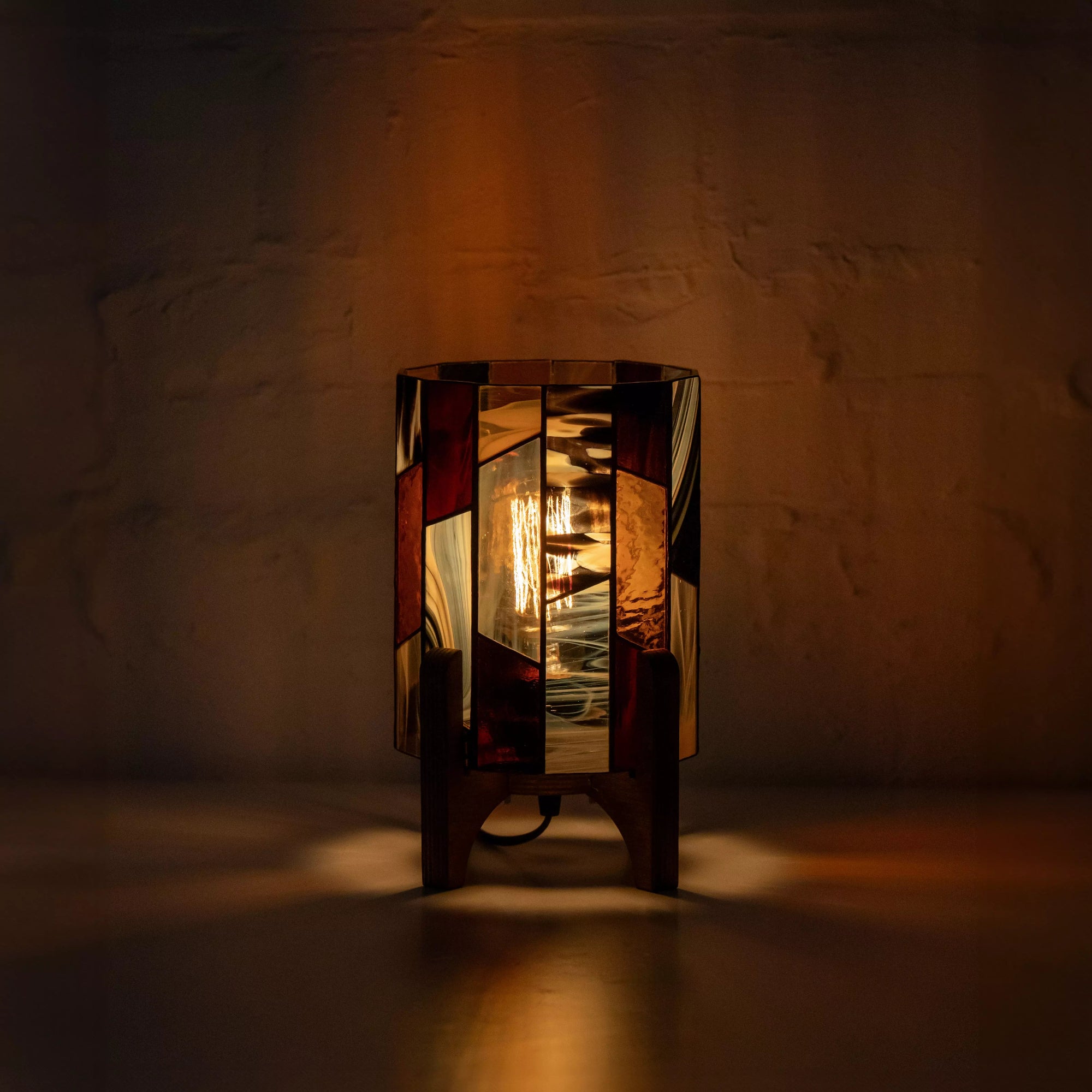 Illuminated stained glass table lamp glowing in the dark, featuring warm amber and bronze tones that create soft ambient lighting.