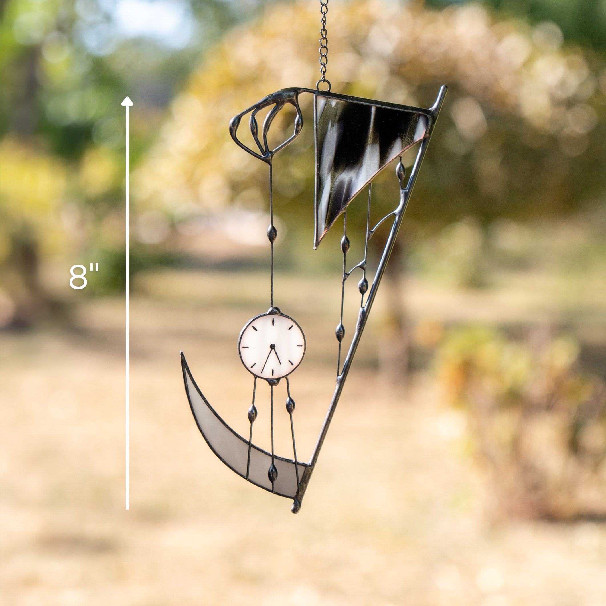 Outdoor photo of stained glass scythe-shaped decor with clock, hanging from suction cup, height marked 8"