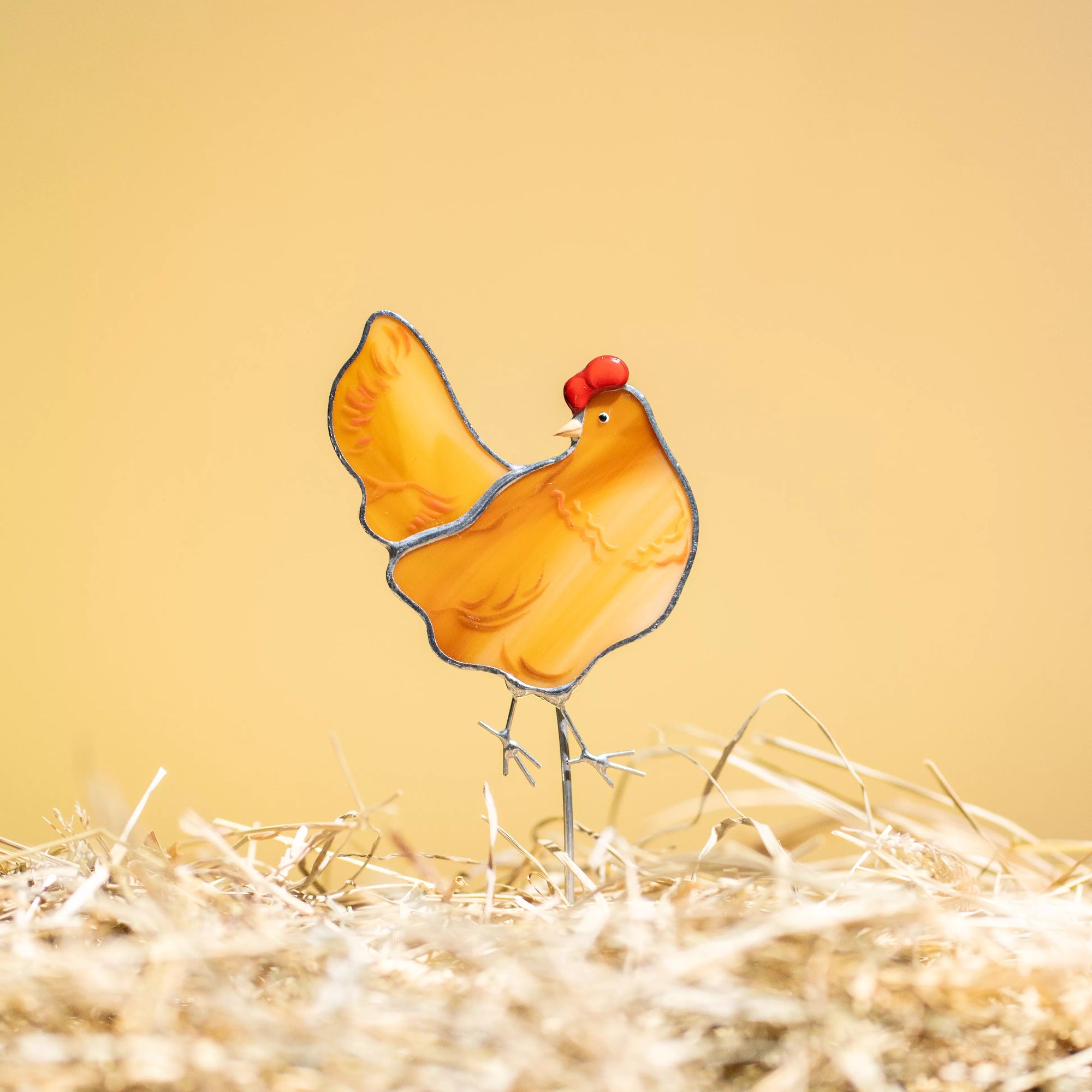 Stained glass chicken plant stake on a bed of straw with a yellow background