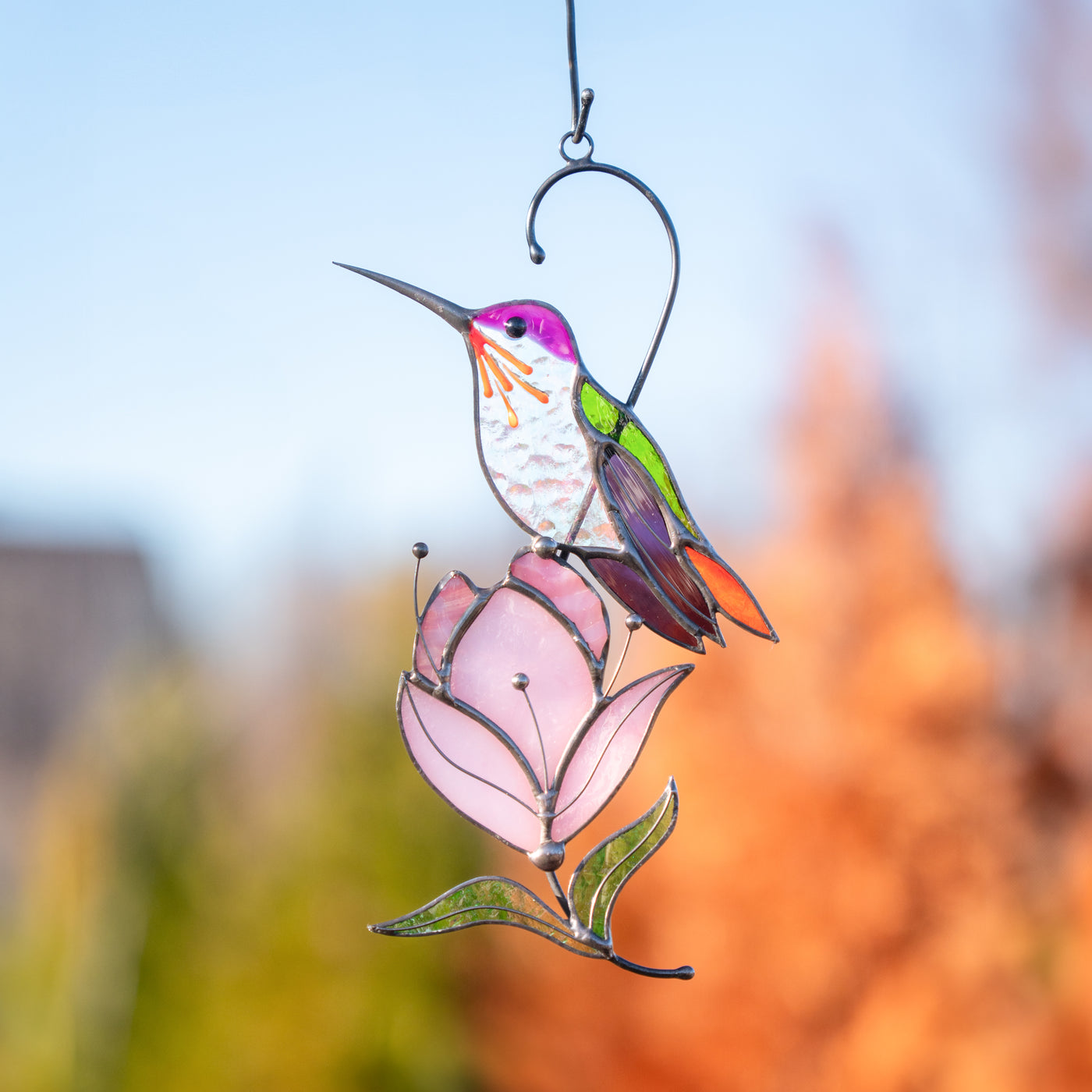 Hummingbird stained glass ornament in vibrant tones perched on magnolia, captured outdoors in golden light.