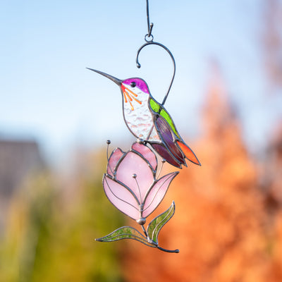 Hummingbird stained glass ornament in vibrant tones perched on magnolia, captured outdoors in golden light.