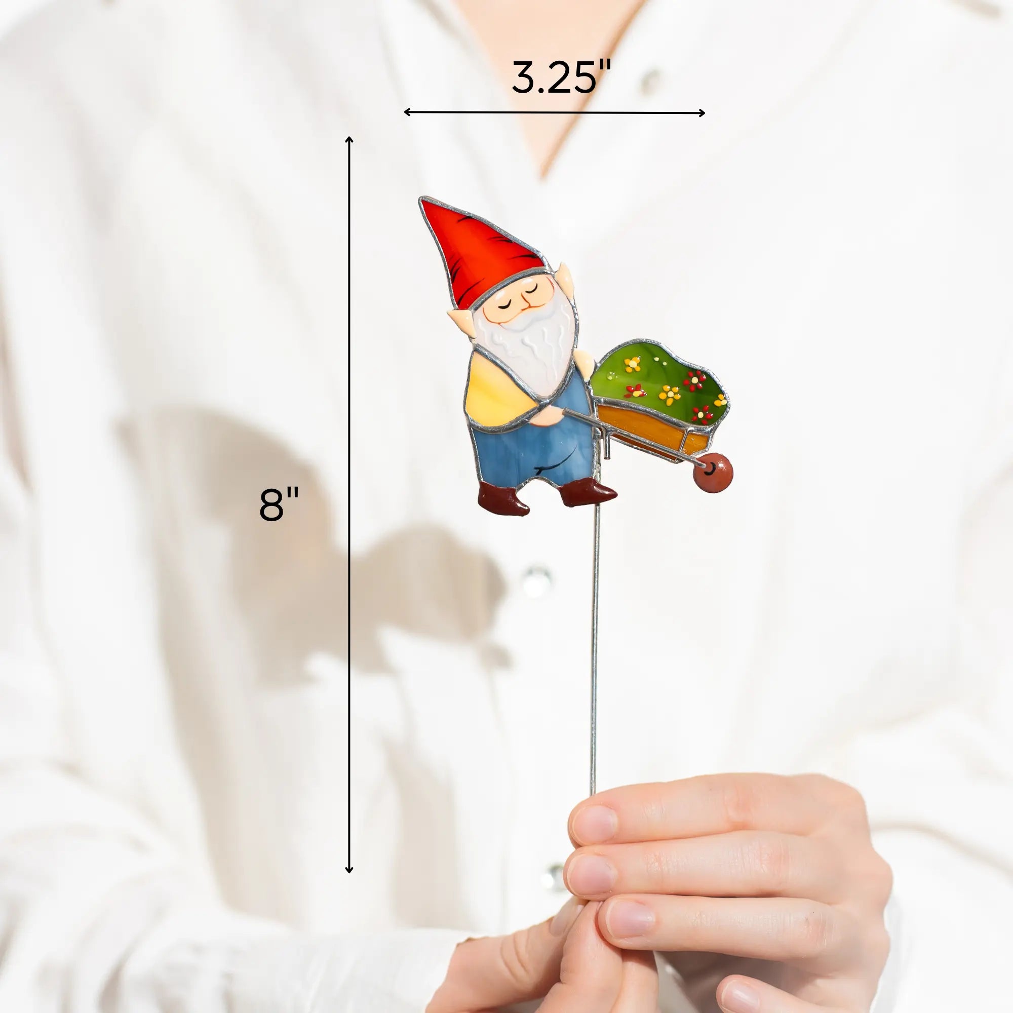 Gnome with a wheelbarrow stained glass plant stake held by a person with measurements indicated 3.25 x 8 inches