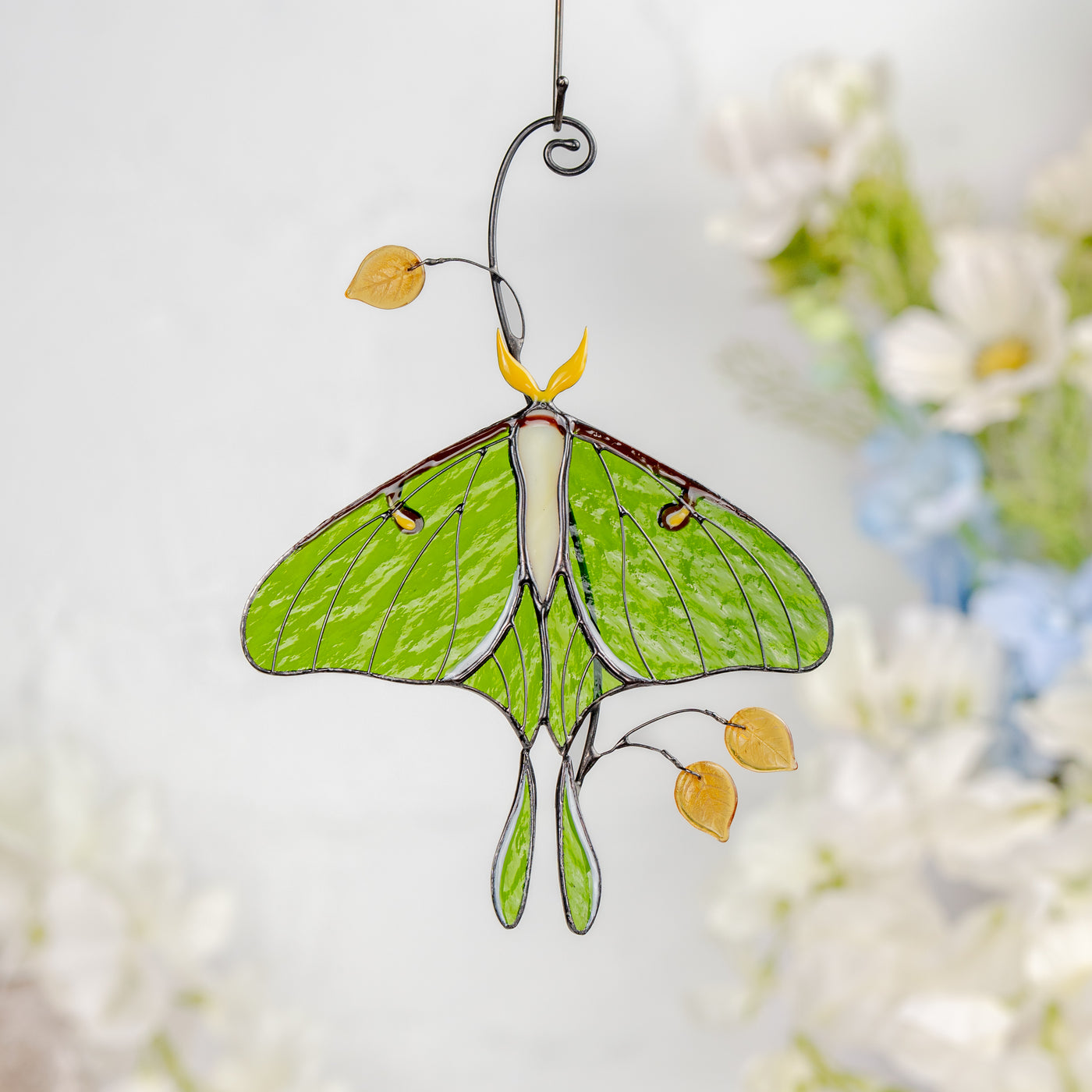 Luna moth stained glass hanging with soft white and blue floral background.