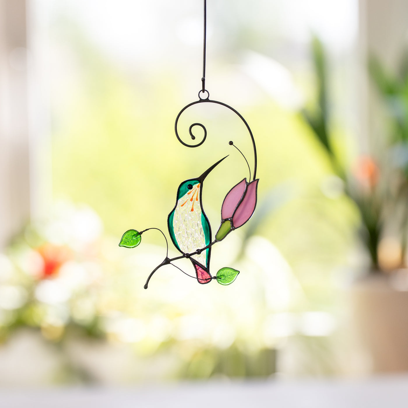 Hummingbird stained glass suncatcher next to a pink flower, perfect for window or garden decoration.