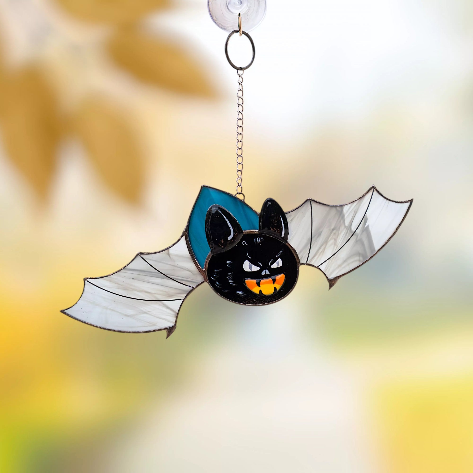 Stained glass bat with white wings and orange pumpkin teeth hanging on window