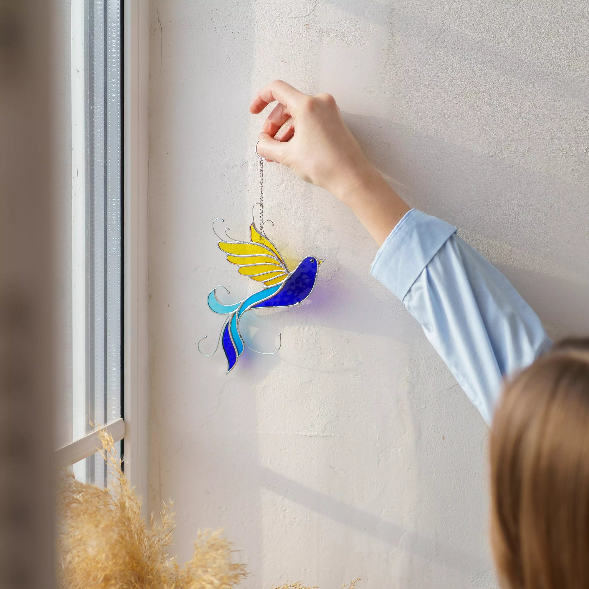 Womens hand holding a colorful glass sun catcher against a window.