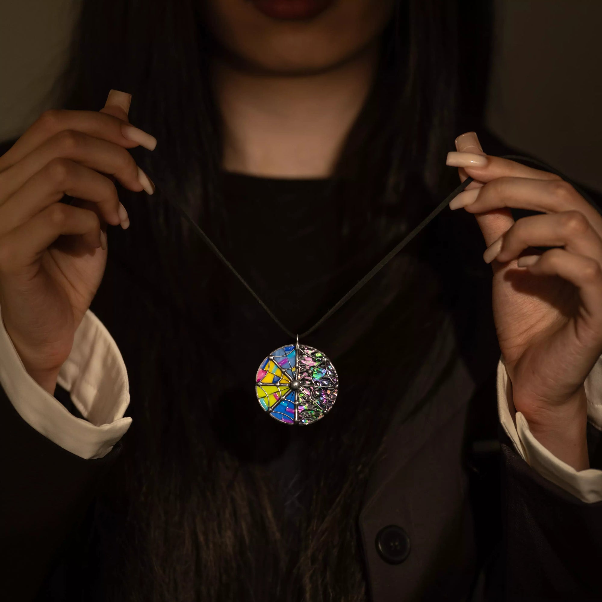 Person holding a colorful irizated stained glass necklace in dark academia style