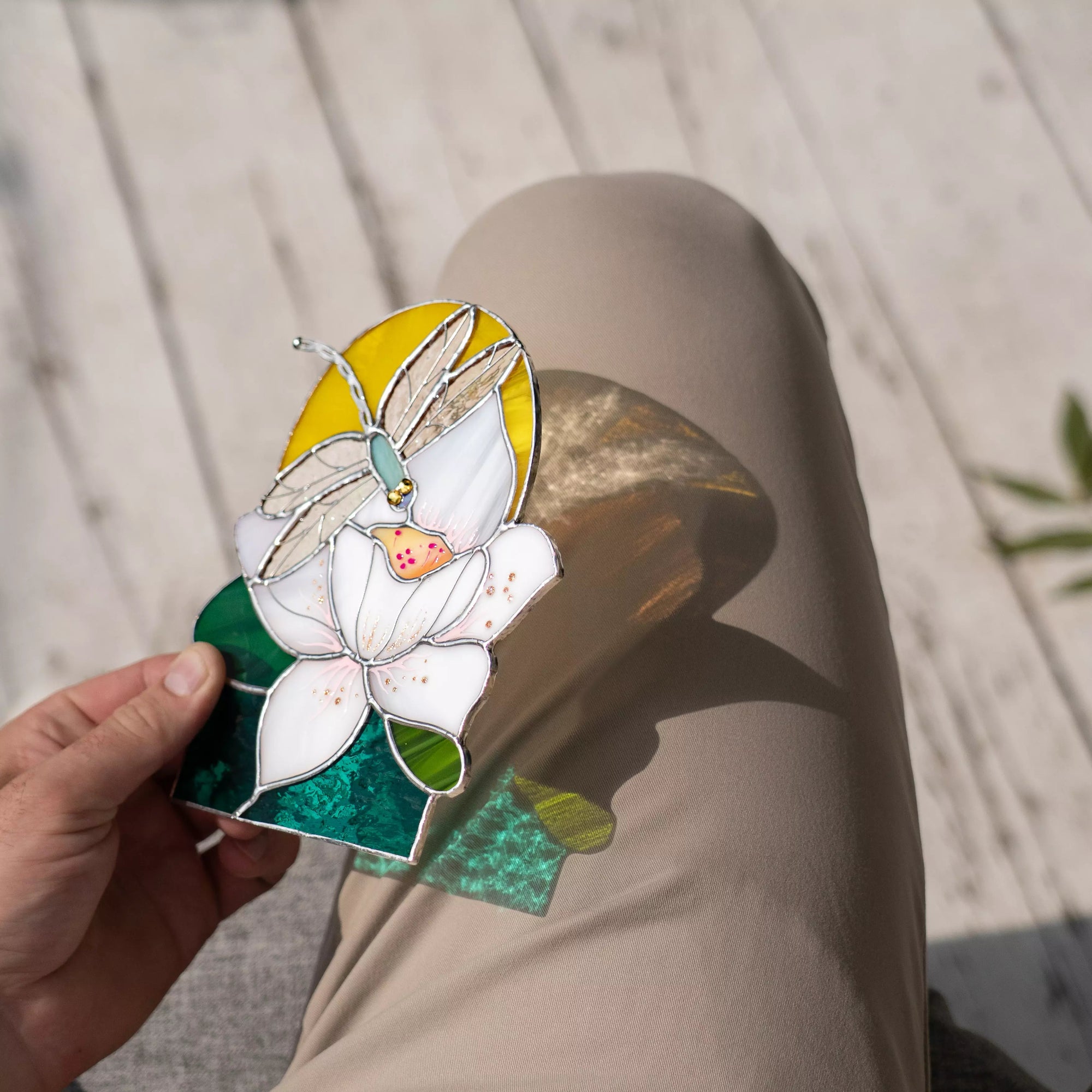 Hand holding a decorative glass panel with a butterfly and flower design, that casts shadow on a wooden surface.