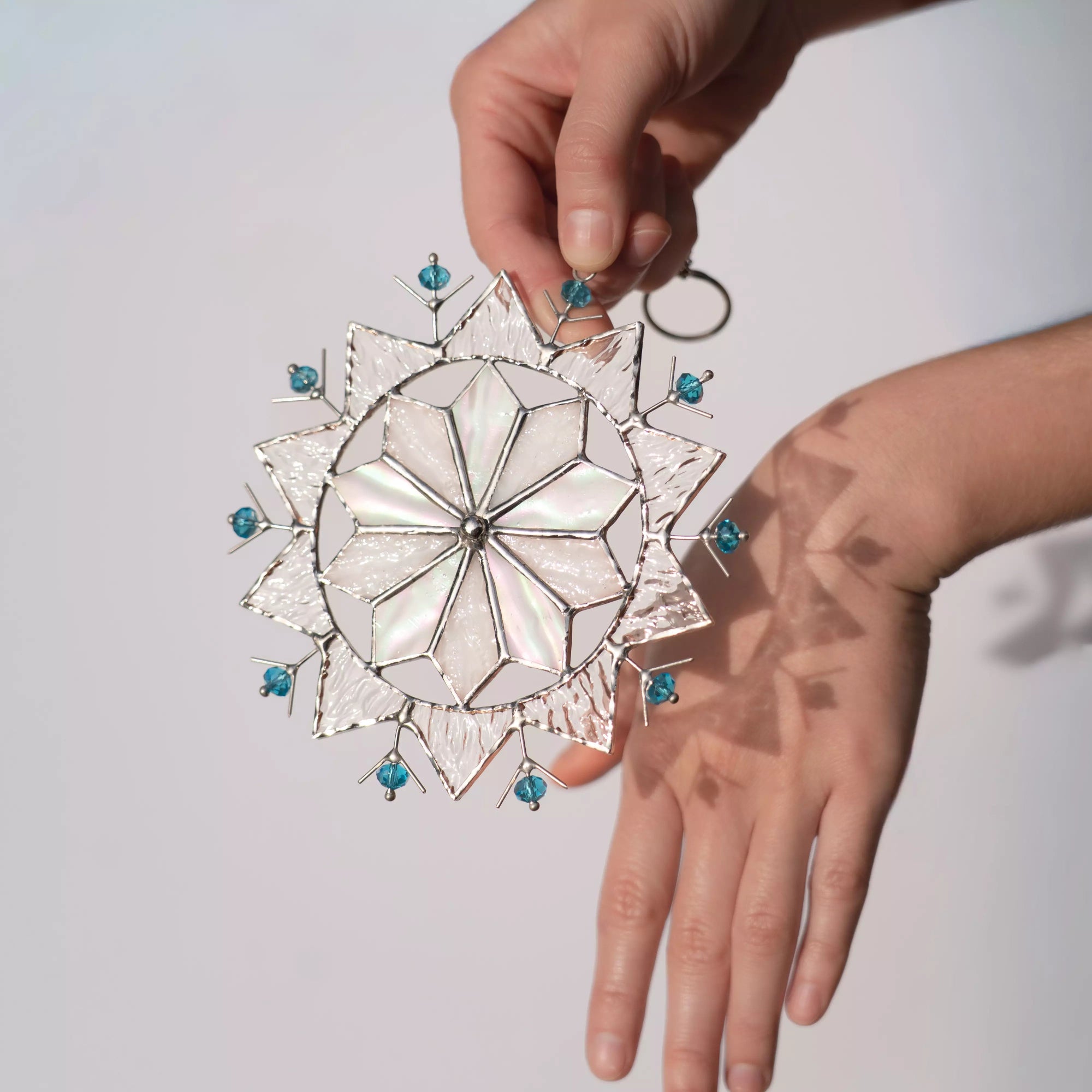 Hand holding stained glass snowflake suncatcher with blue beads against a light background