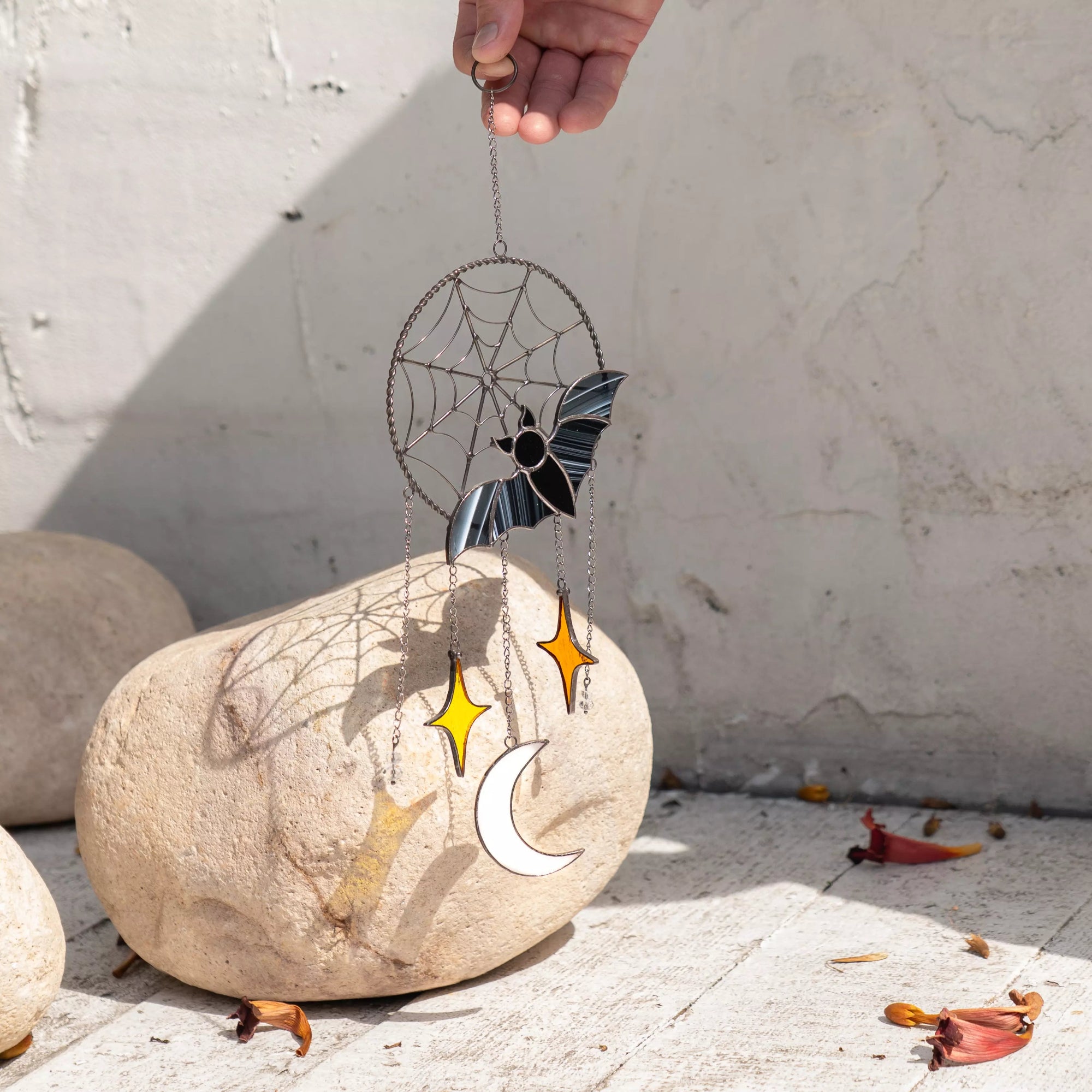 Hand holding a decorative wind chime with celestial elements casting colorful shadow on a stone surface.
