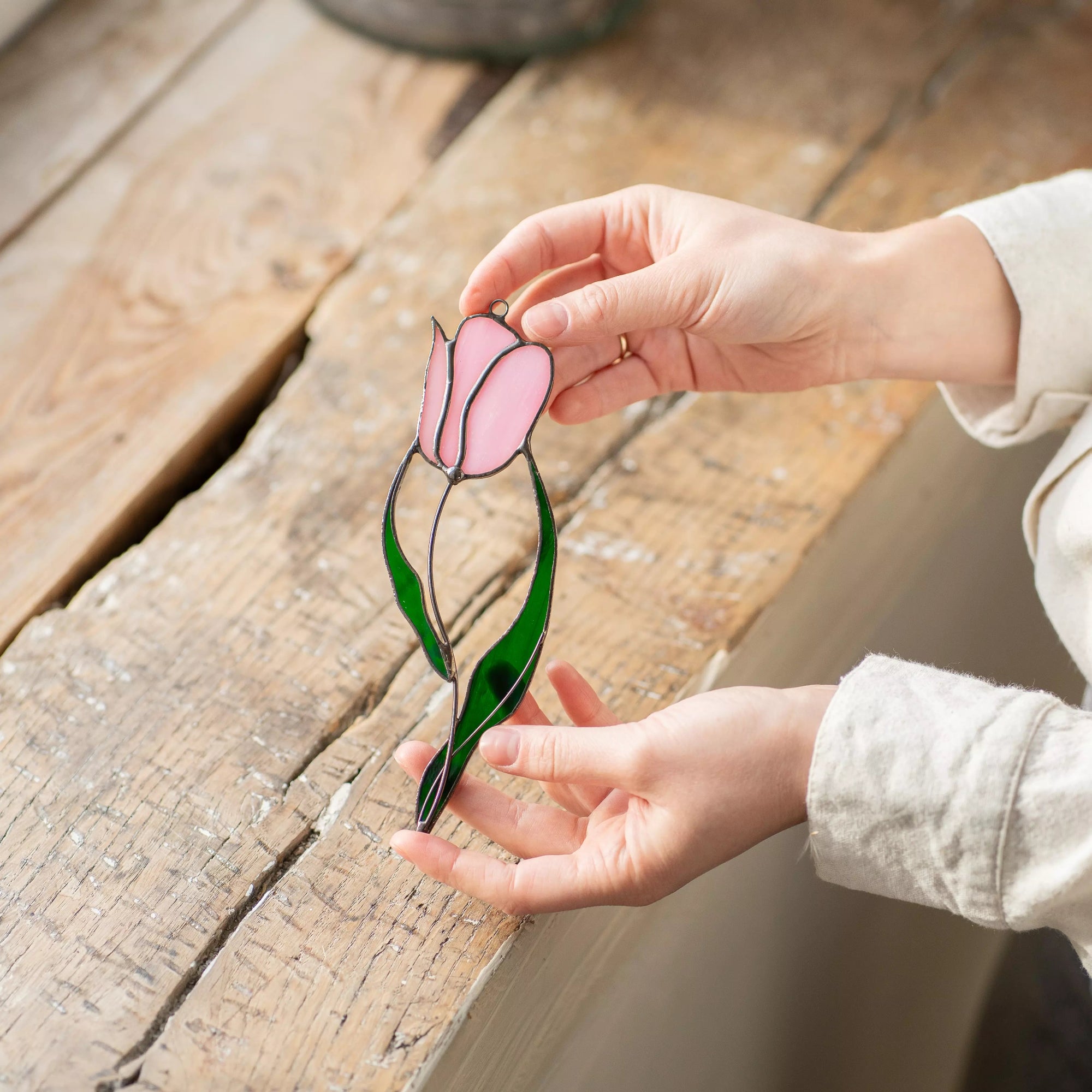 Hand holding a stained glass suncatcher pink and green stained glass tulip on a wooden surface