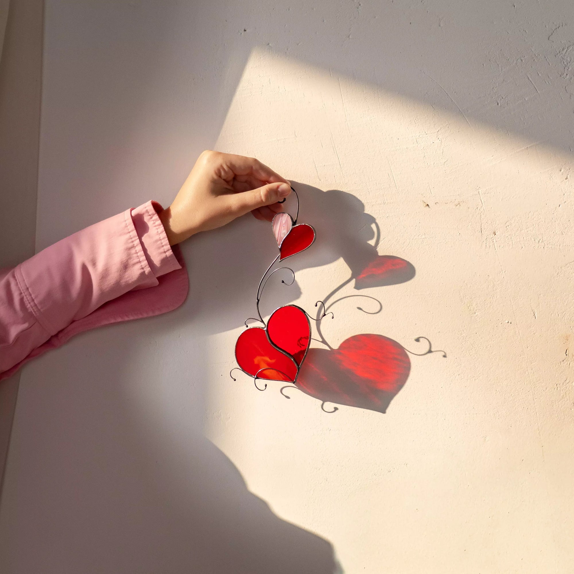 Hand holding a stained glass suncatcher featuring two hearts and casting a colorful shadow