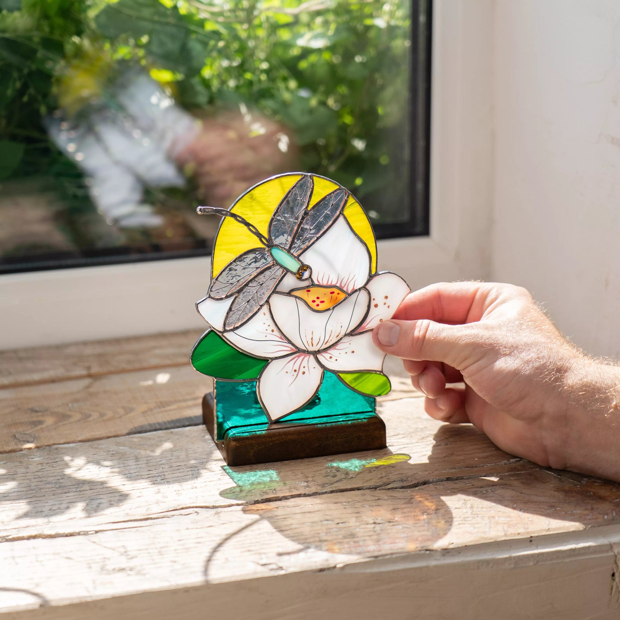 Hand holding a stained glass dragonfly on a lotos flower candle-lit panel