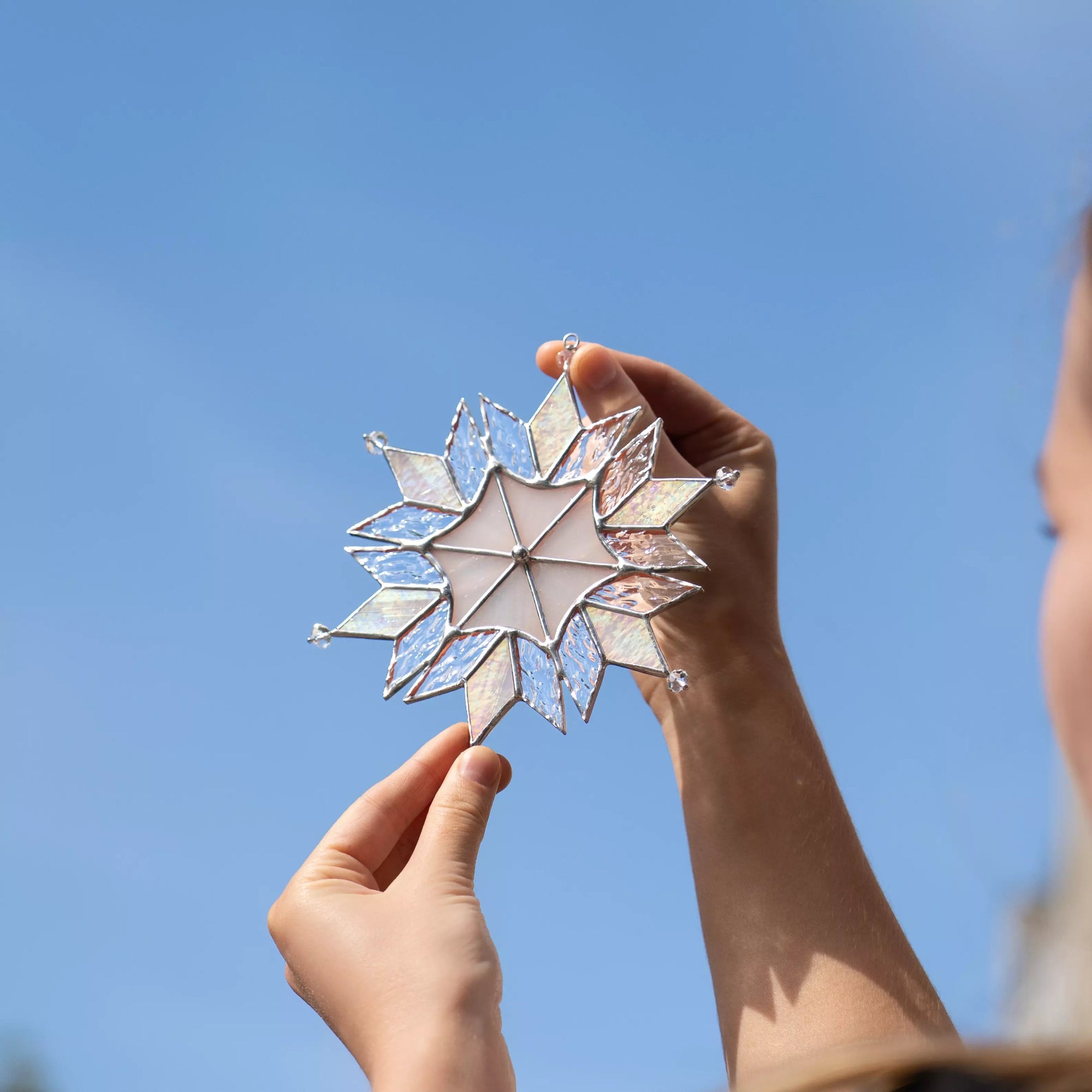 Person holding a stained glass snowflake Christmas ornament against a clear blue sky
