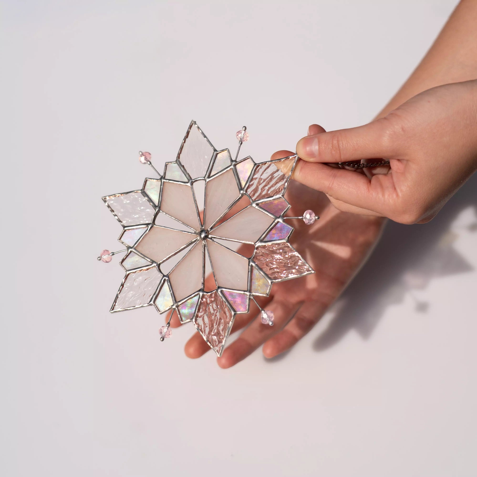 Hand holding a stained glass snowflake ornament, that casts soft shadow against another hand and light background