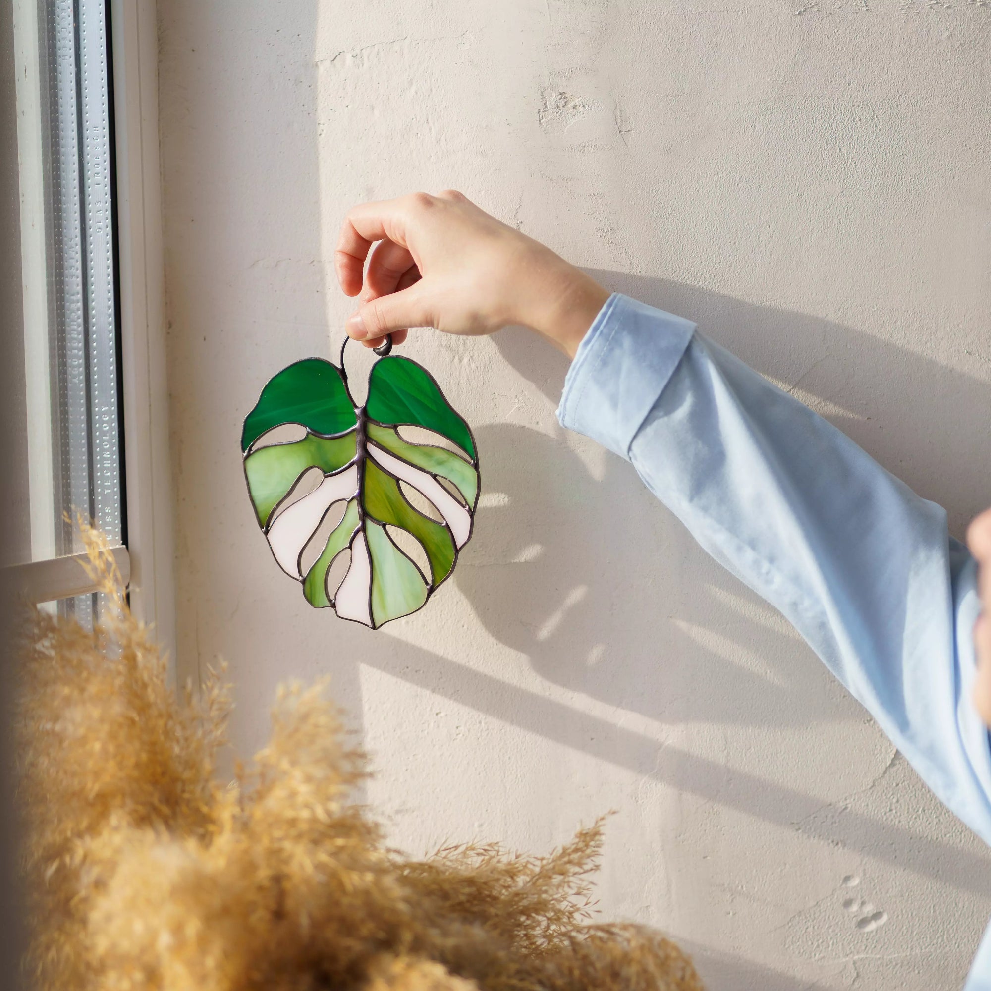 Hand holding stained glass suncatcher monstera leaf casting a soft shadow on a wall