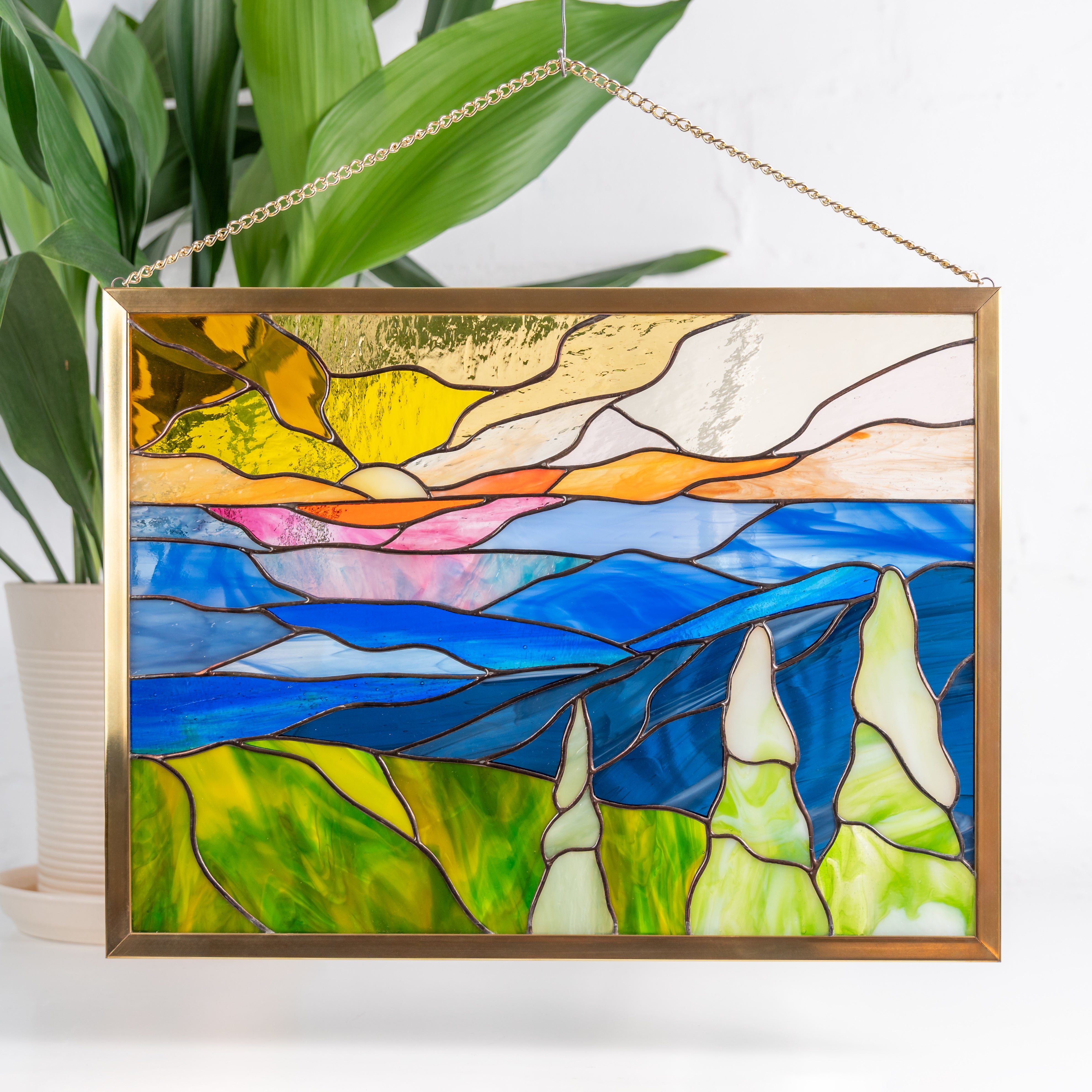 Blue Ridge mountain stained glass panel hanging indoors in front of plant, vibrant and nature-inspired